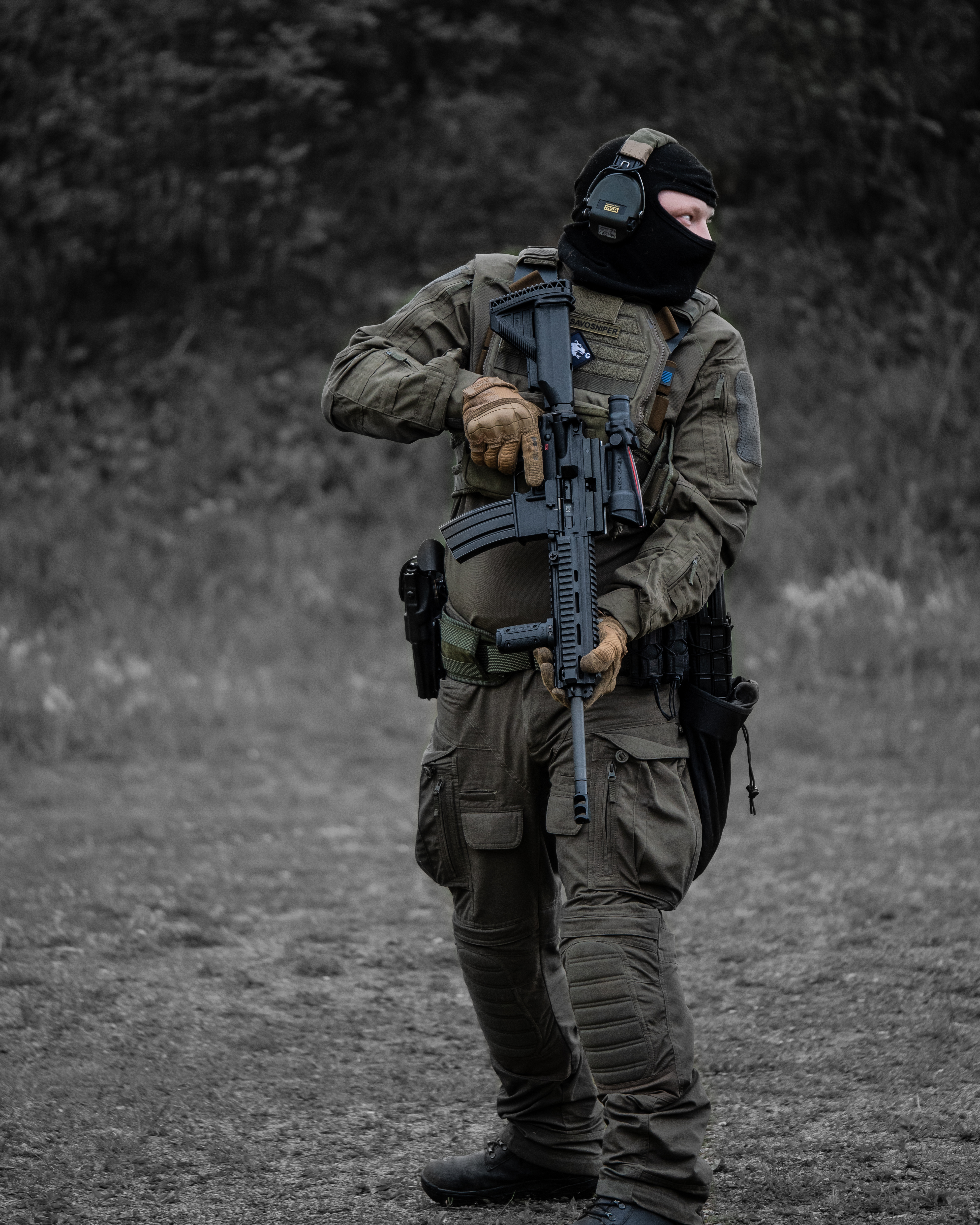 Man with a balaclava, headphones, earpro uf pro combat shirt, uf pro tactical pants, gunbelt and a plate carrier is turning around with a rifle M4 heckler & koch 416 with a ACOG optic in hand. He is on a shooting range. He is doing a shooting drill.  Finnish reservist