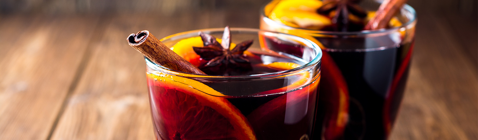 Two glasses of mulled wine with oranges and spices on wooden background