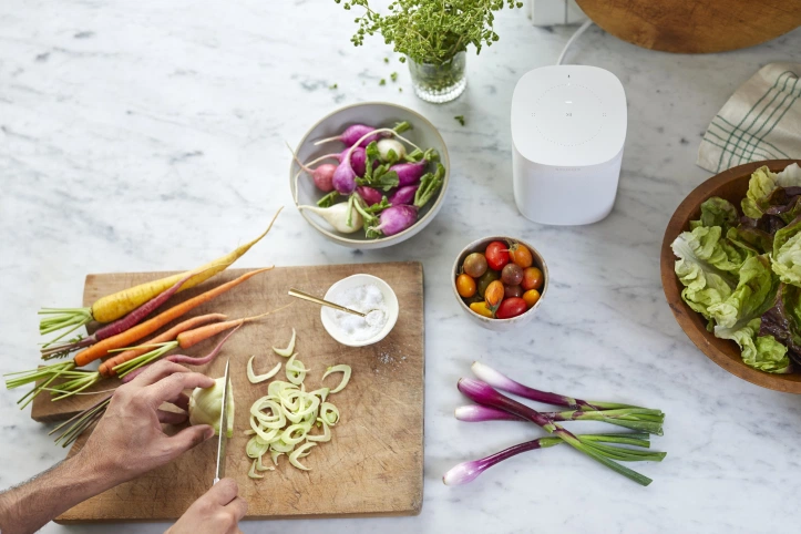 Sonos One on a kitchen table top while a person cuts vegetables