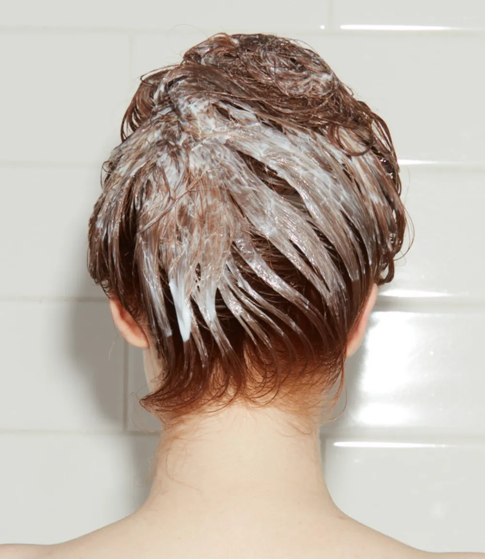 Woman in shower with conditioner coating her hair