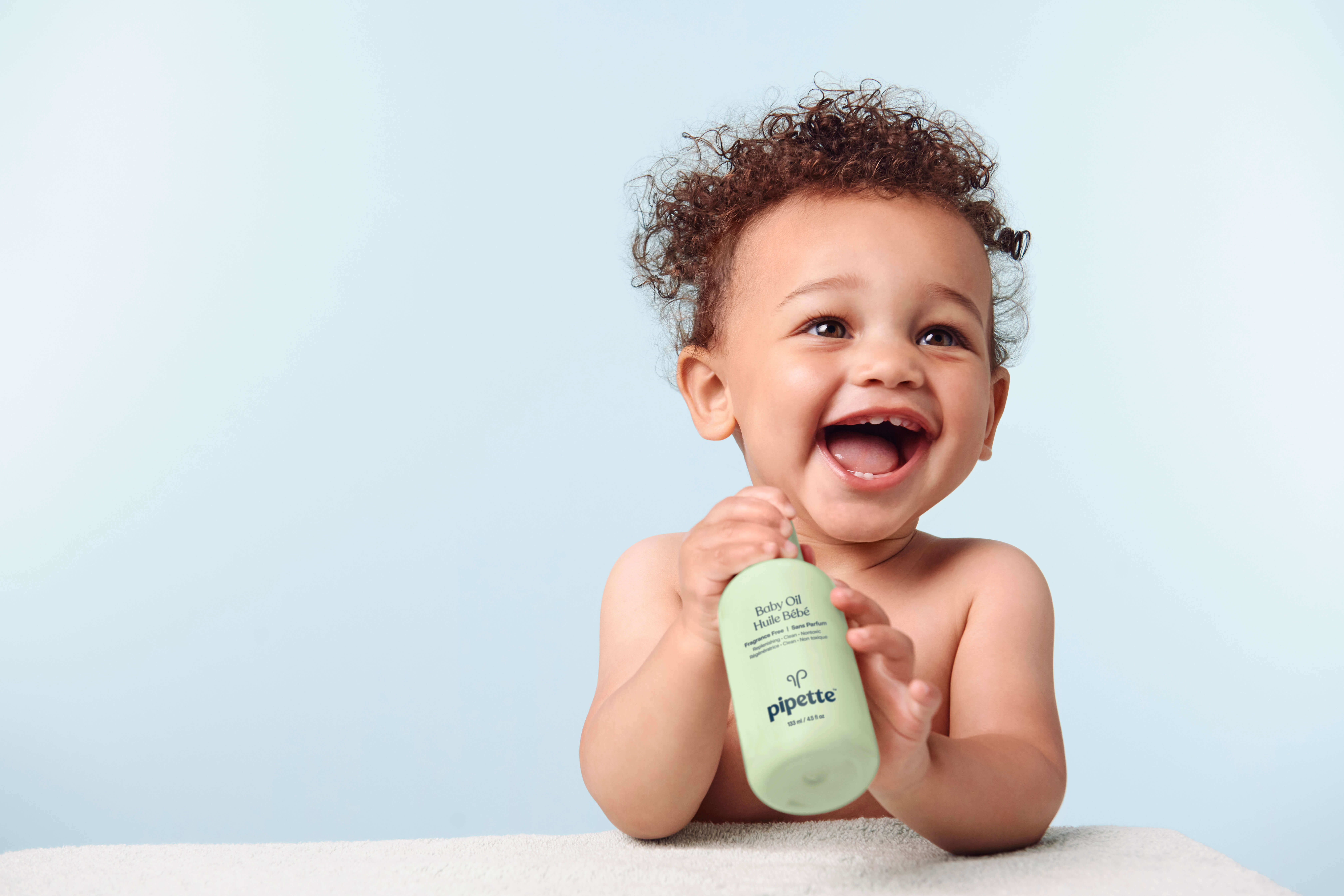 Baby smiling and holding Baby Oil.