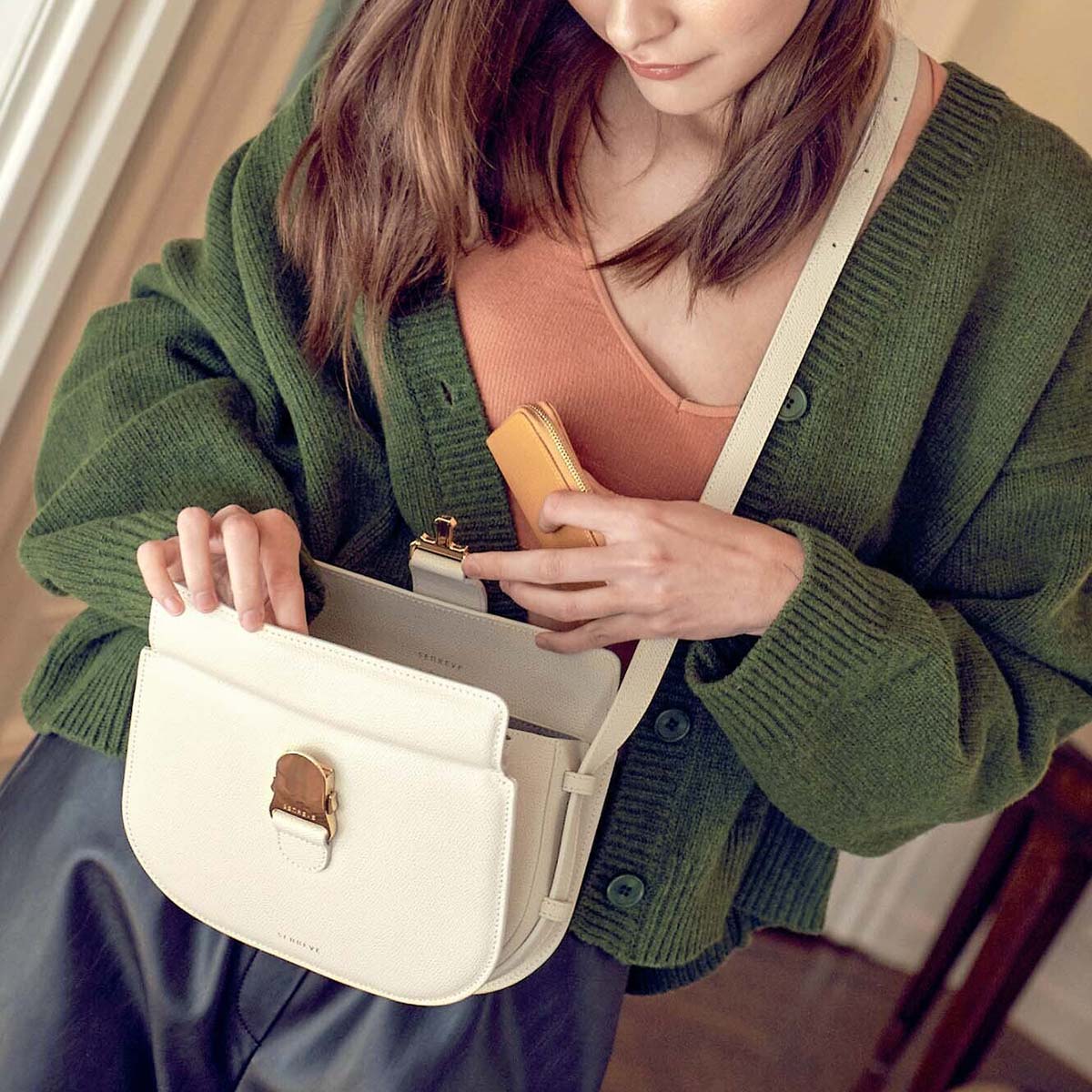 brunette woman wearing a white crossbody bag with the bag open