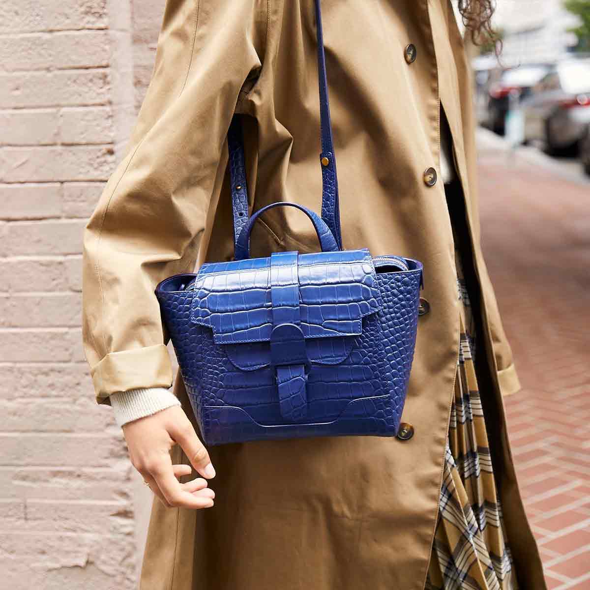 Mini Maestra Bag Marine with Gold Hardware Interior Side, Shown on Shoulder of Woman with Pale Skin weaning a Tan Burberry Trench Coat