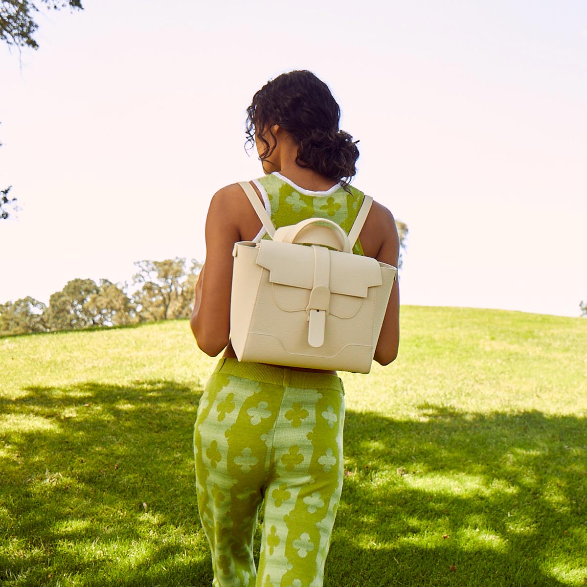 Woman in lime green outfit wearing Midi Maestra as a backpack walking in a bright green field
