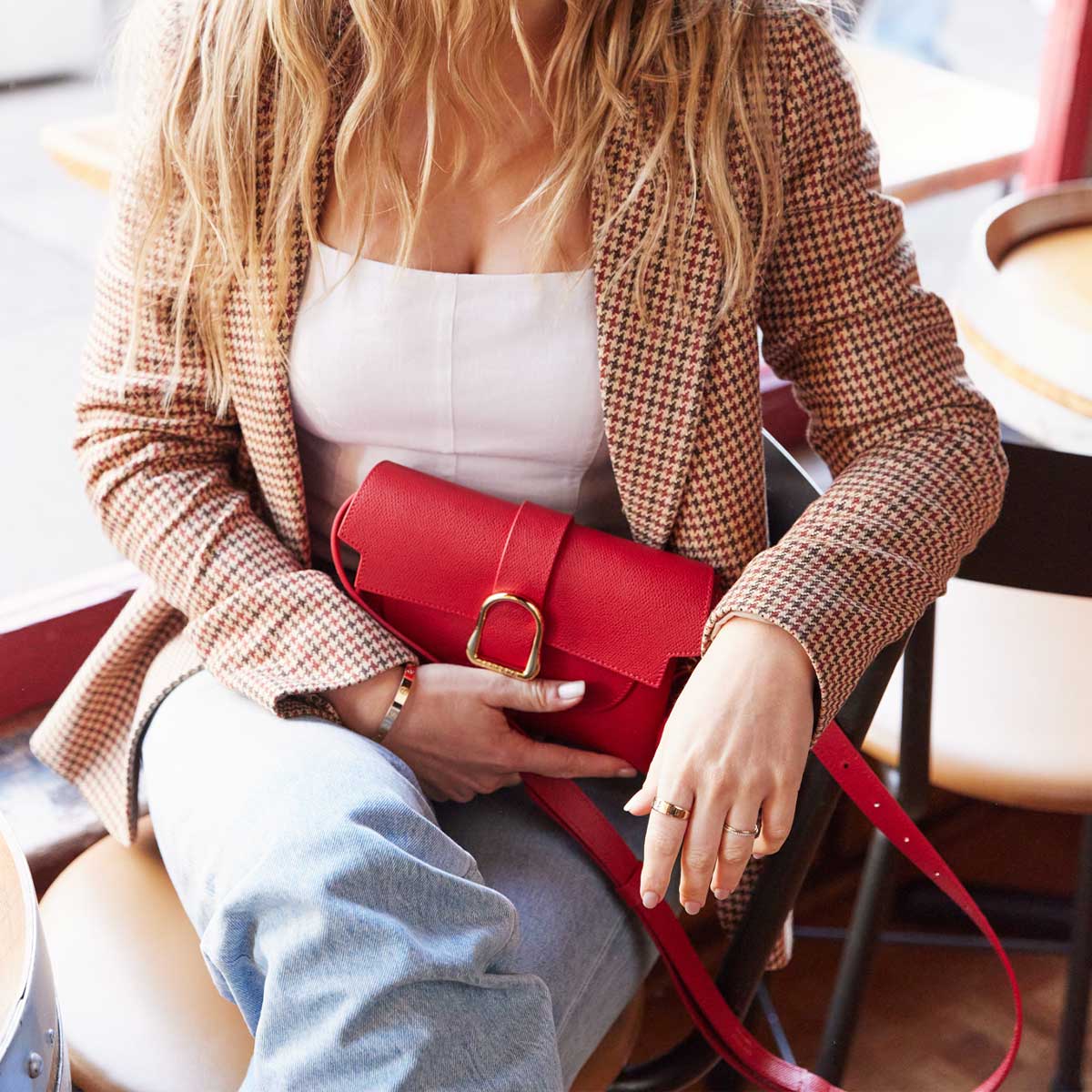 blonde woman wearing a plaid blazer holding a red leather belt bag