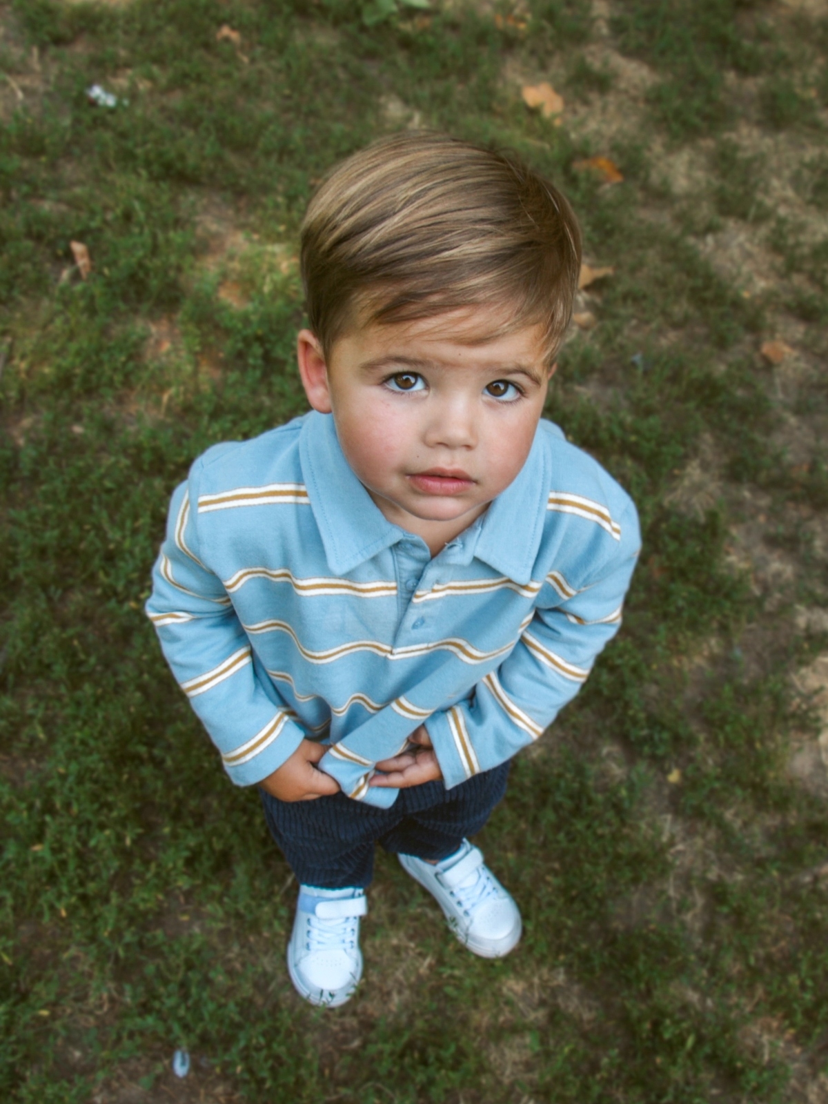 young boy wearing striped polo in grass