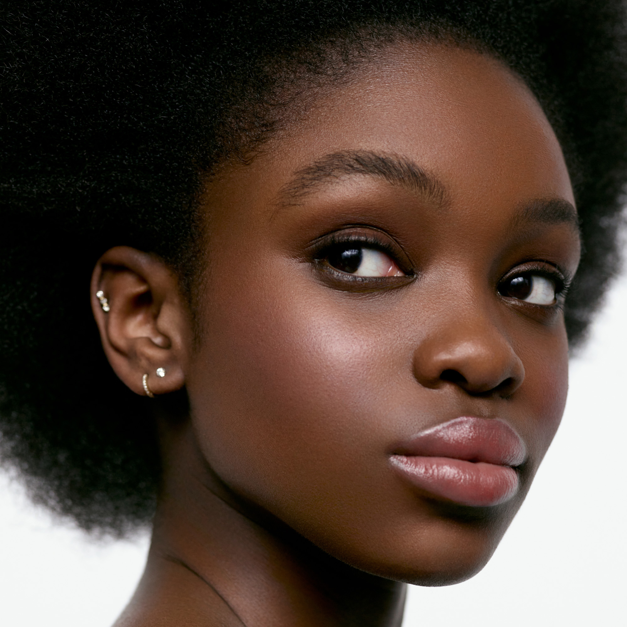 Image of a deep skin tone model wearing the Cream Blush Refillable Cheek & Lip Color in Heliotrope 1