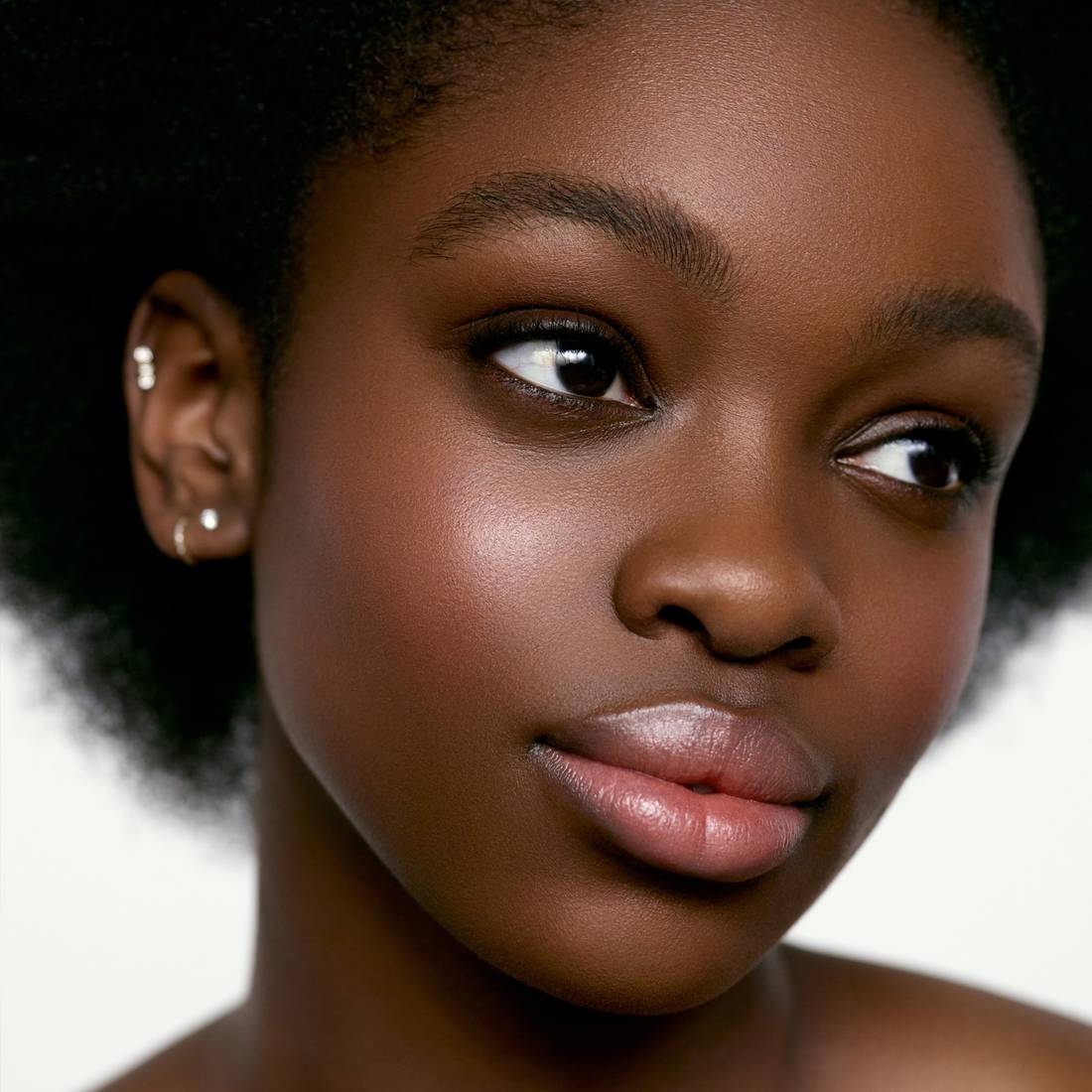 Image of a deep skin tone model wearing the Cream Blush Refillable Cheek & Lip Color in Anemone 1