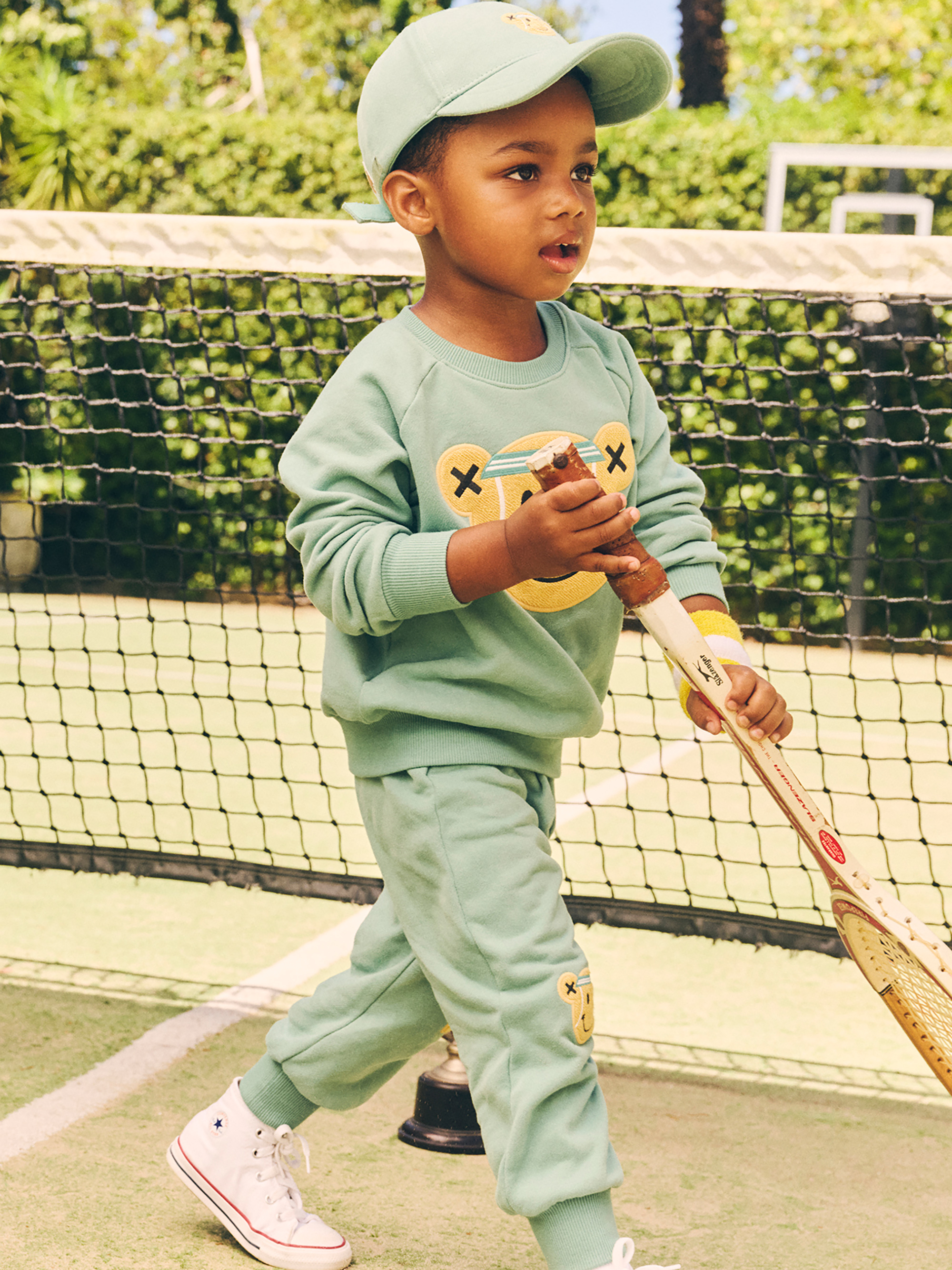 boy wearing huxbaby tennis bear set in tennis court