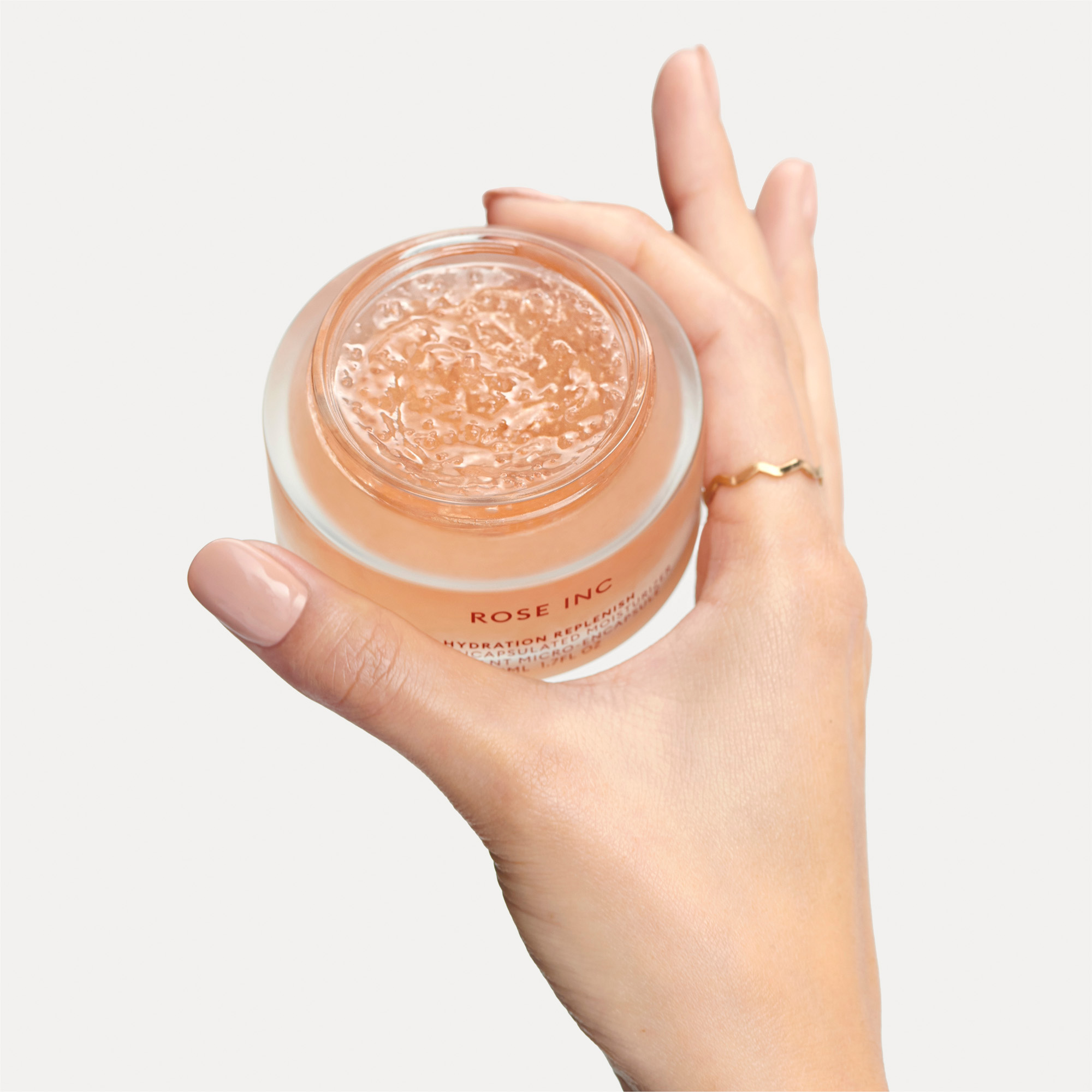 Image of a female hand holding the Hydration Replenish Moisturizer so you can see the microencapsulated beads and formula's texture