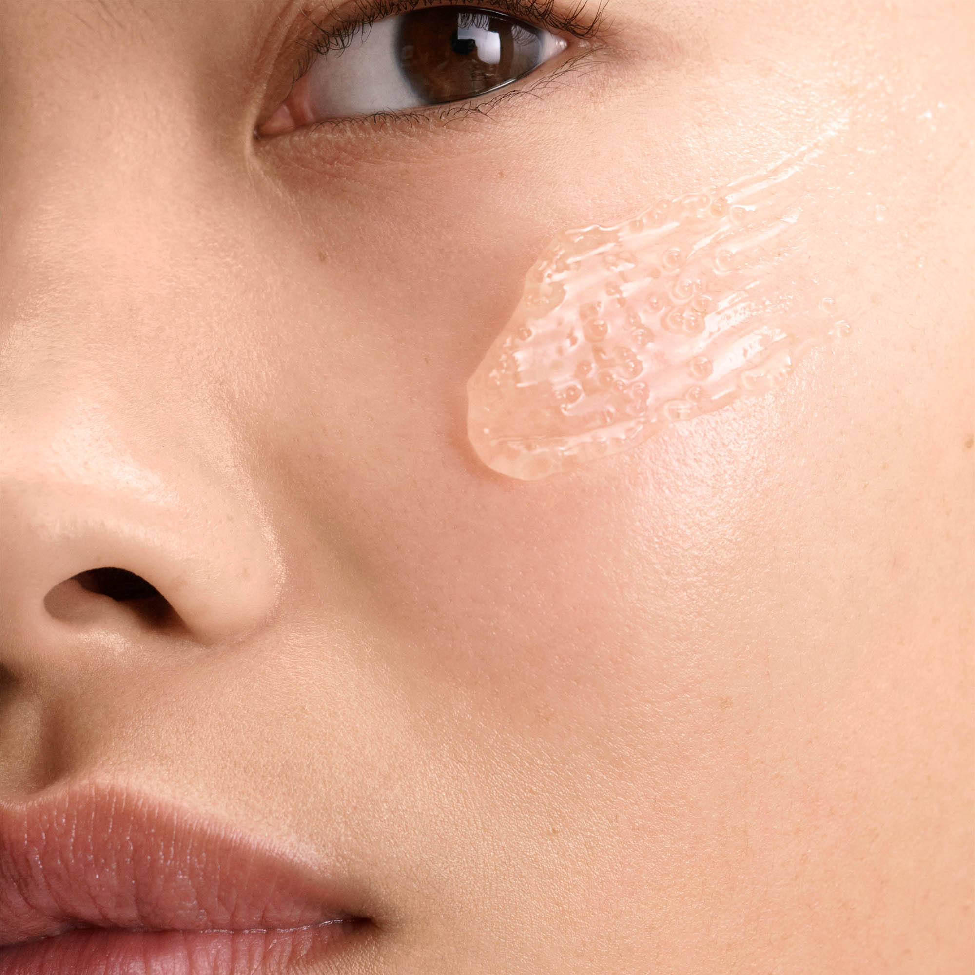 Close up model image of her face with a swipe of the moisturizer on her cheek to show the microencapsulated beads