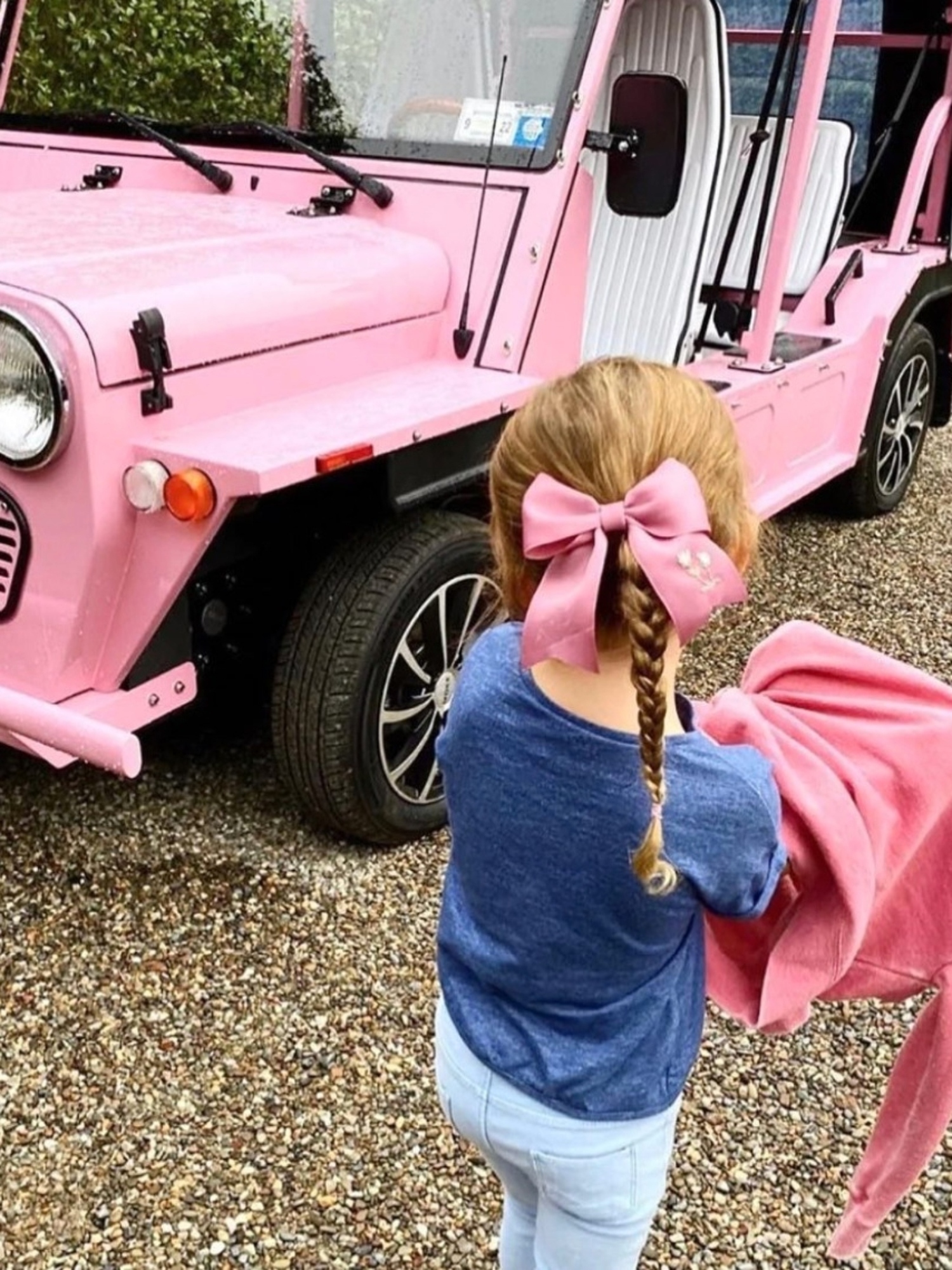 young girl in front of pink car wearing pink hair bow