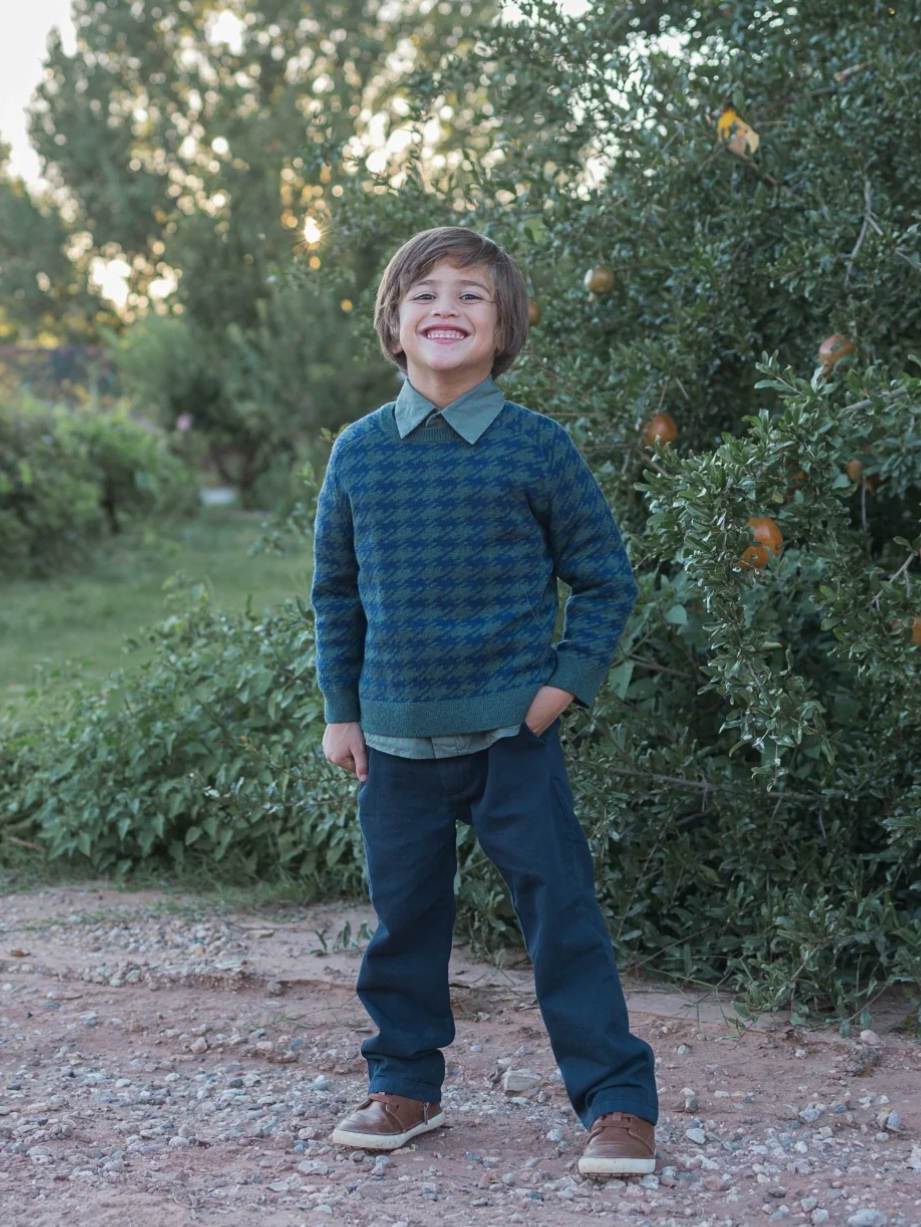 young boy wearing sweater and pants surrounded by trees