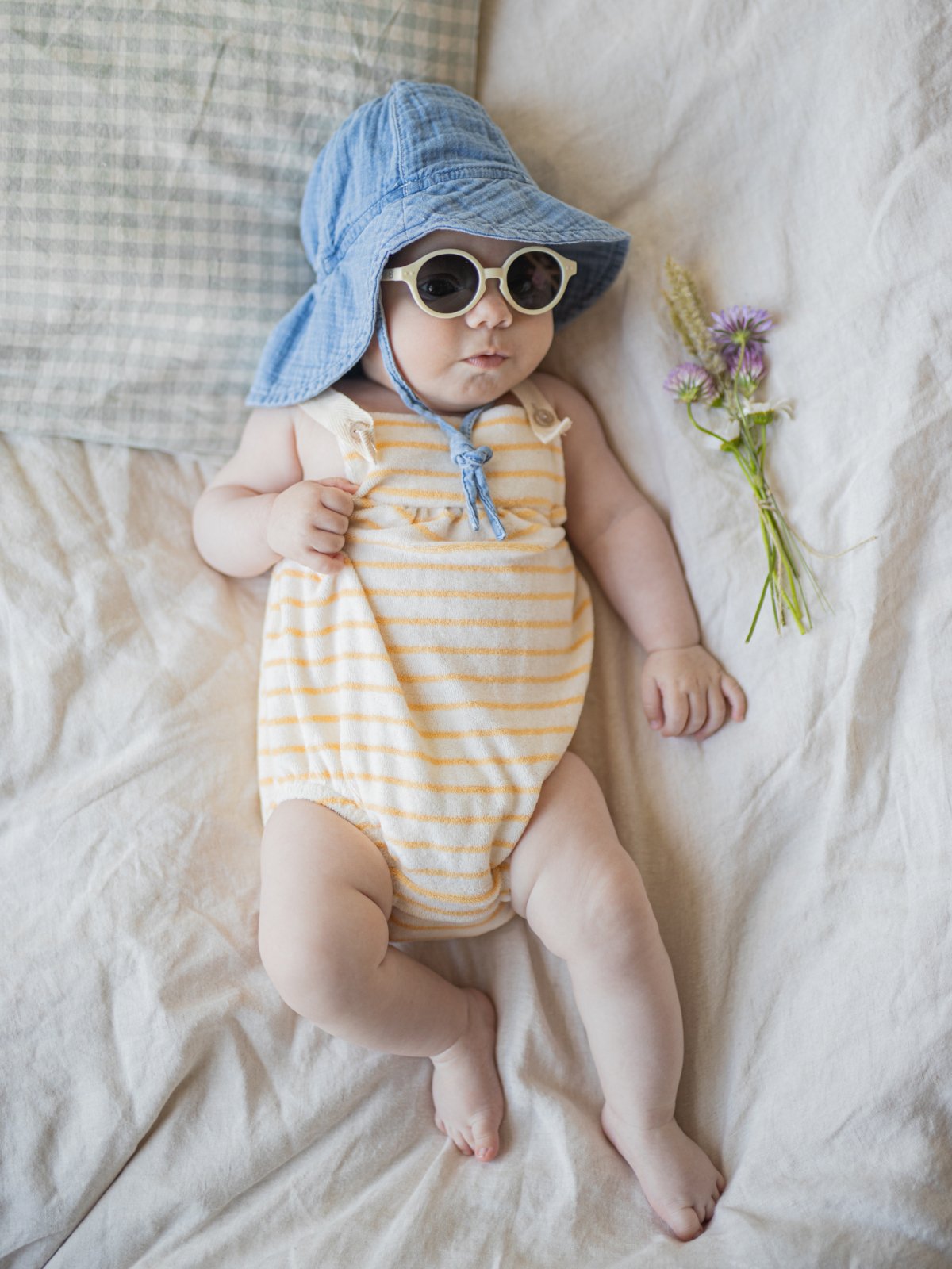Smiling baby wearing a yellow striped onesie, lying on a white blanket.