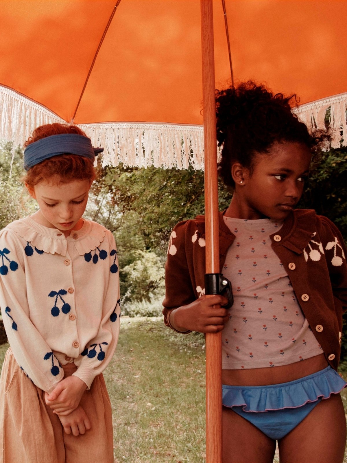 two young girls standing under orange beach umbrella