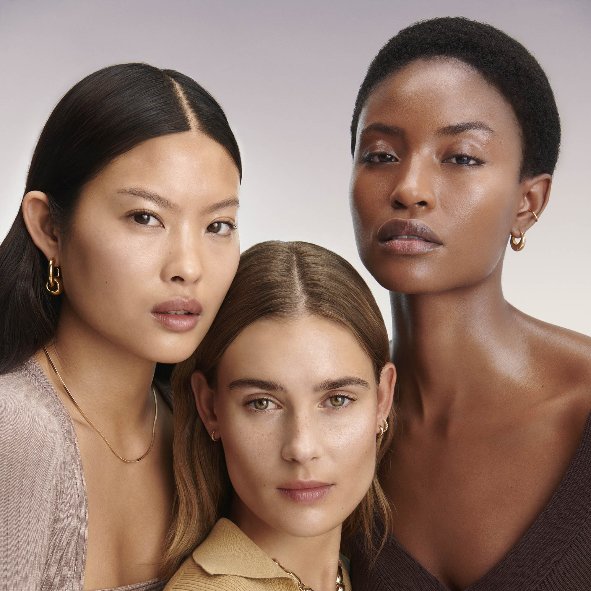 Image of a medium skin tone (left), light skin tone (center) and deep skin tone (right) models posed together each wearing the Rose Inc. Skin Enhance Luminous Tinted Serum.