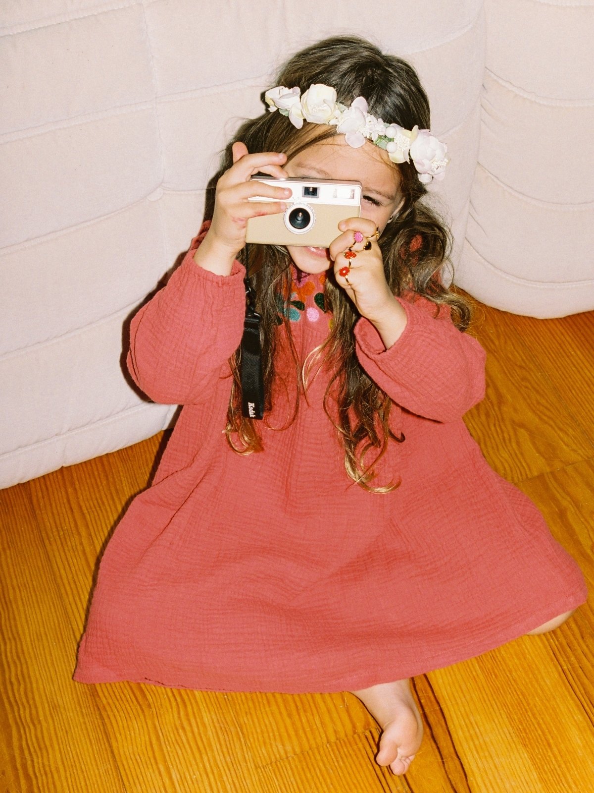 young girl wearing red dress holding camera up to her face