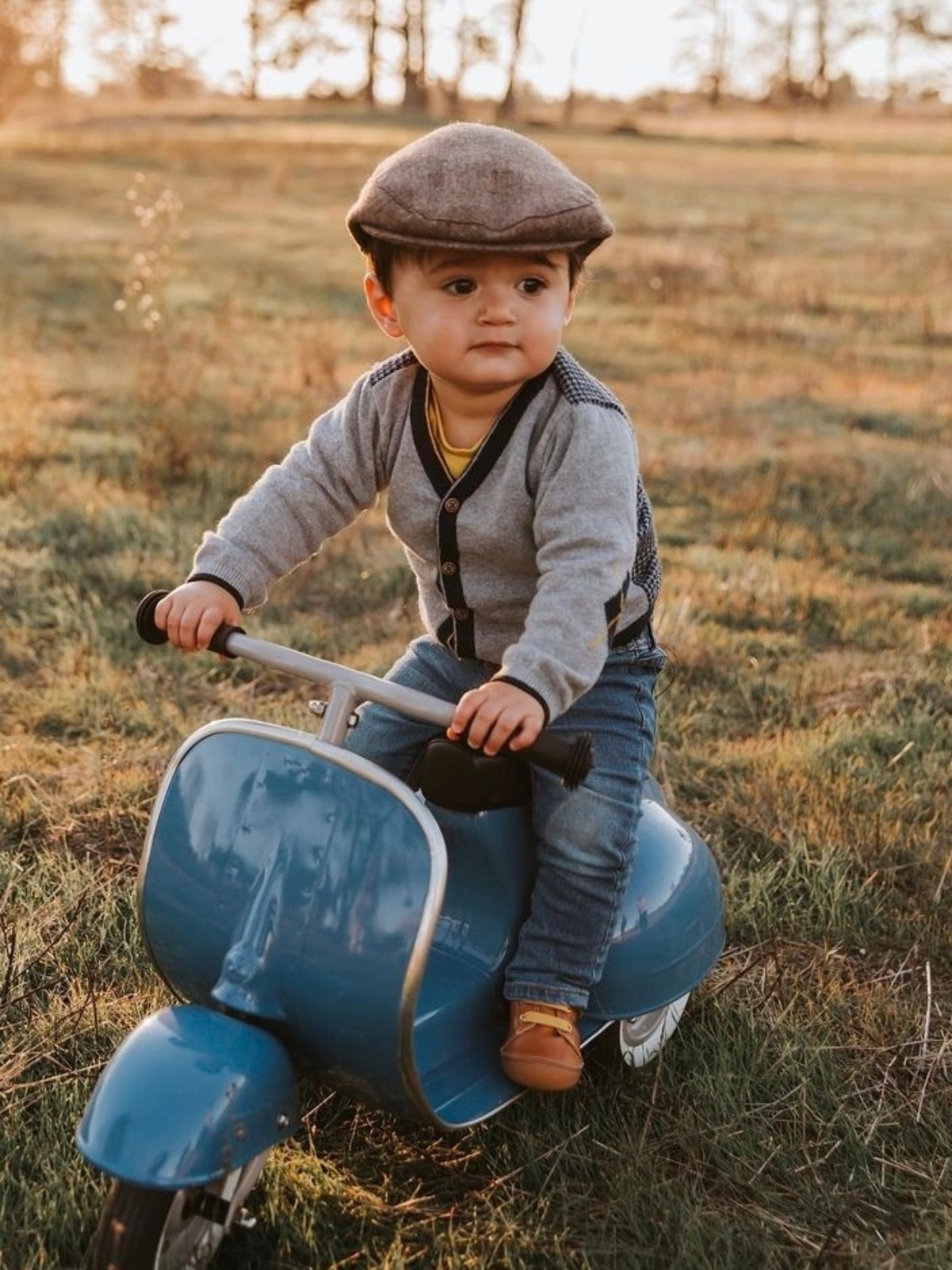 young boy riding blue amboss scooter in field of grass