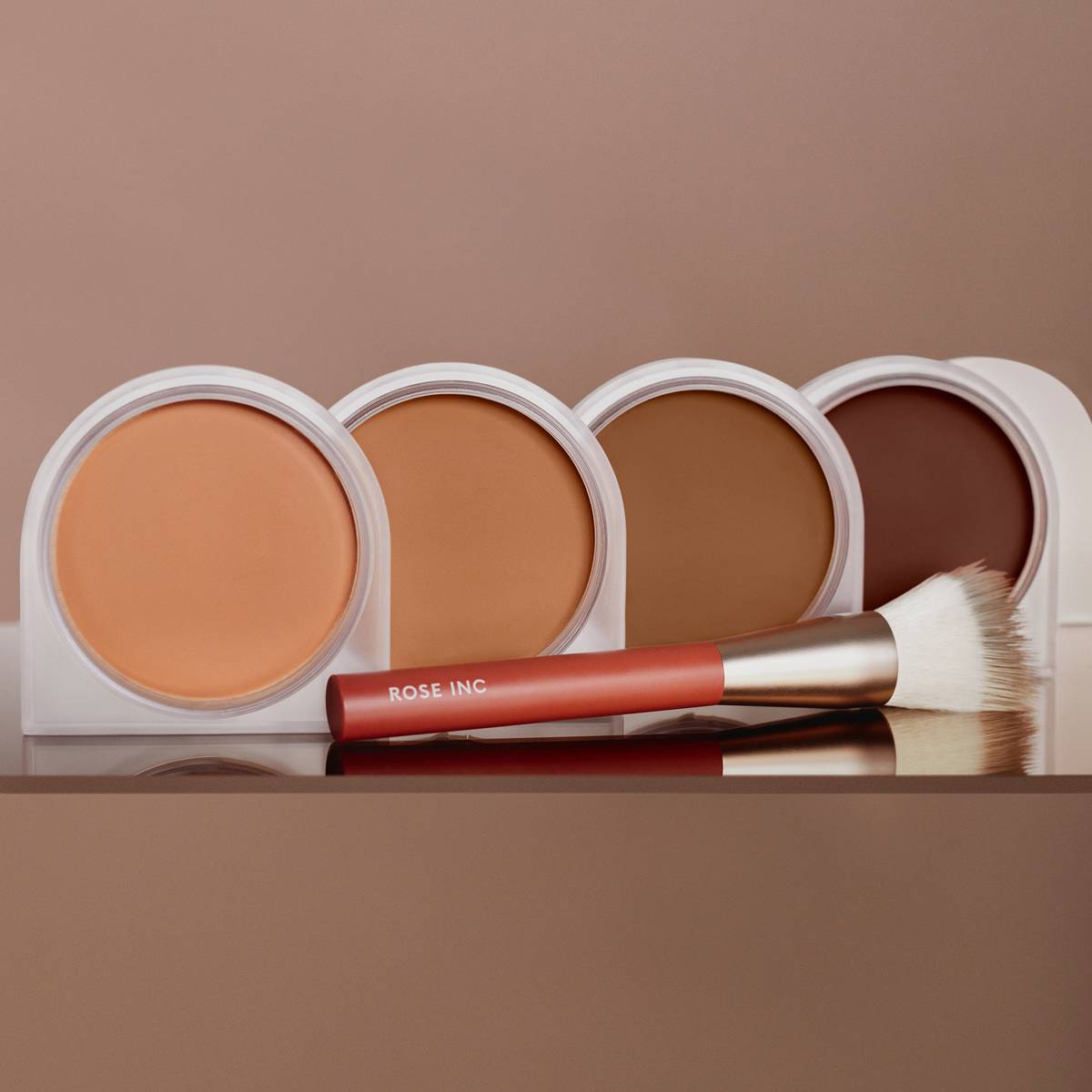 Image featuring each shade of the Solar Infusion Soft-Focus Cream Bronzer lined up in a row with the Number 5 Bronzer Brush laid across the front. 