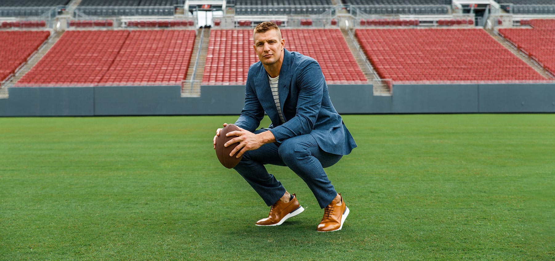 Rob Gronkowski squatting on a football field wearing hybrid dress shoe Crossover™ Longwing in Honey