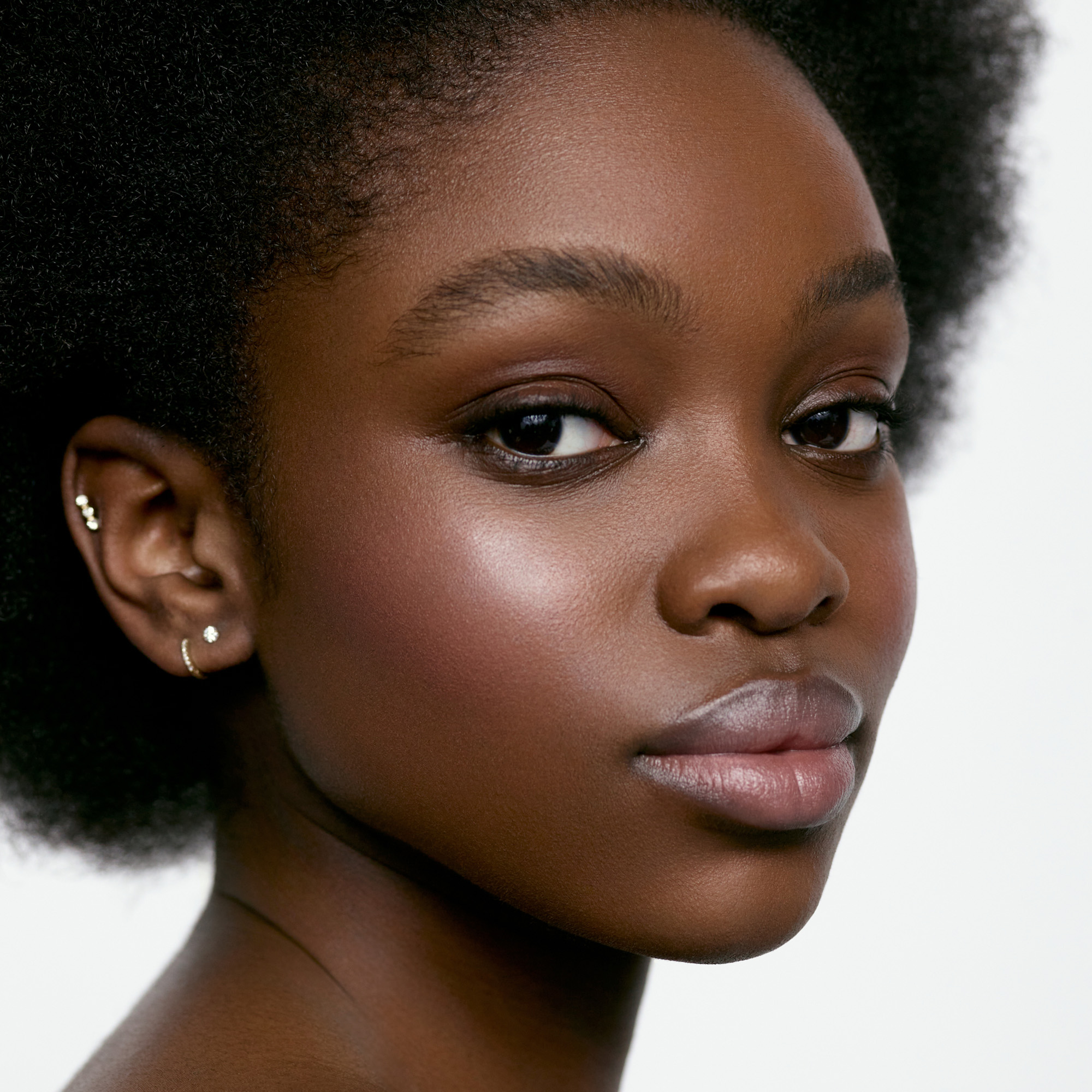 Image of a deep skin tone model wearing the Cream Blush Refillable Cheek & Lip Color in Camellia 1