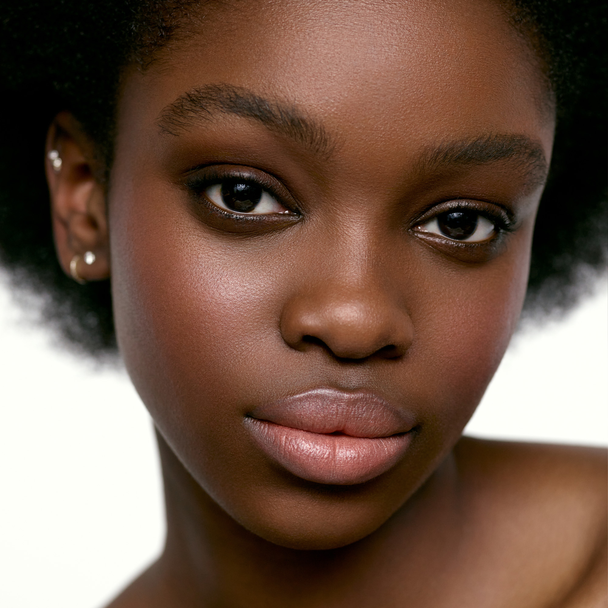 Image of a deep skin tone model wearing the Cream Blush Refillable Cheek & Lip Color in Delphine 1