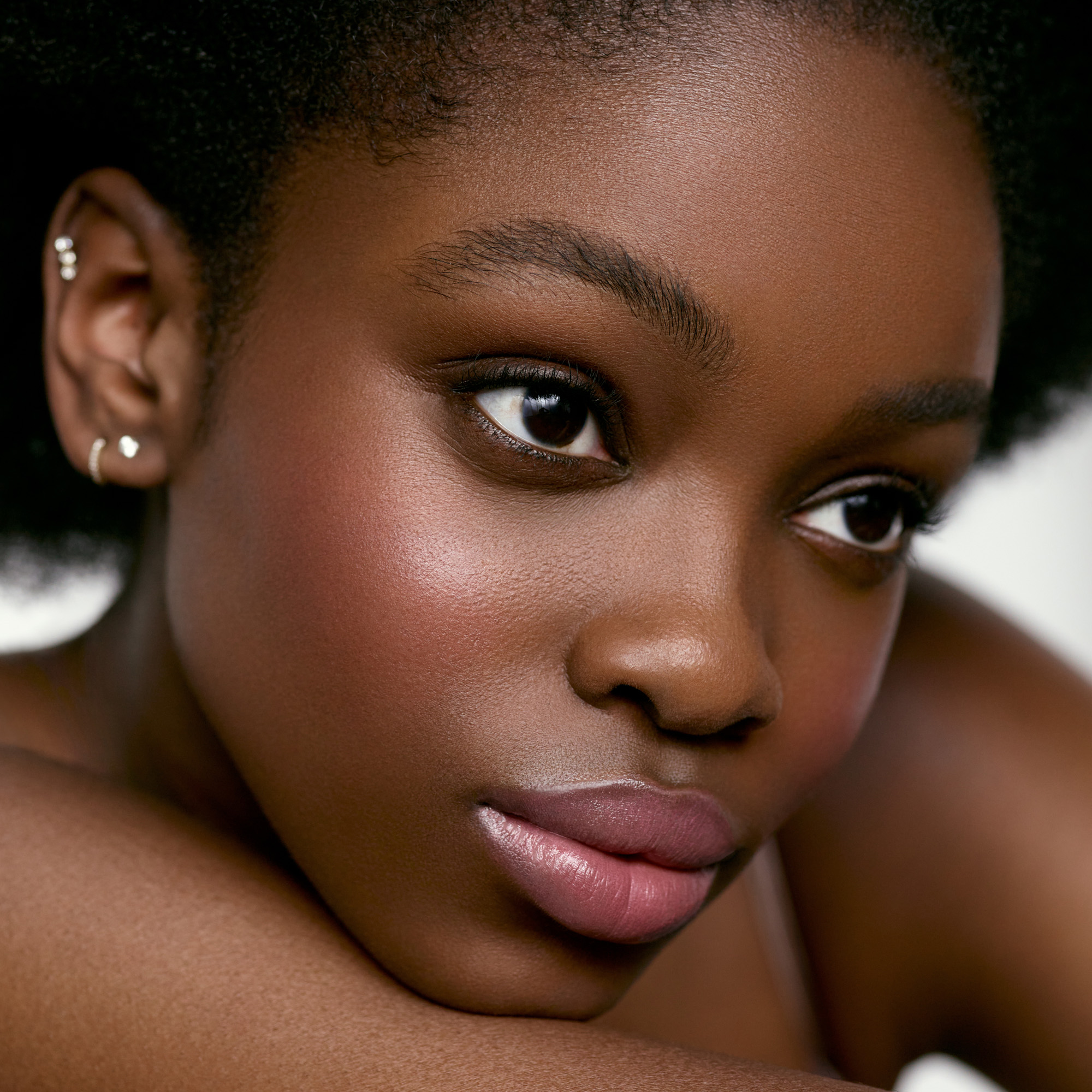 Image of a deep skin tone model wearing the Cream Blush Refillable Cheek & Lip Color in Hibiscus 1