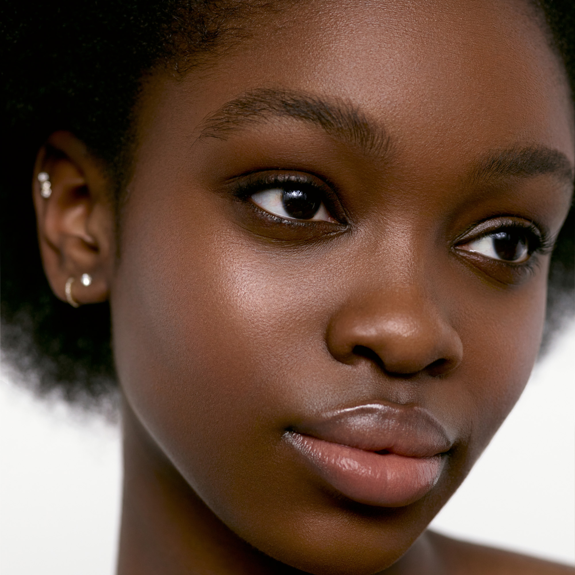 Image of a deep skin tone model wearing the Cream Blush Refillable Cheek & Lip Color in Delphine 1