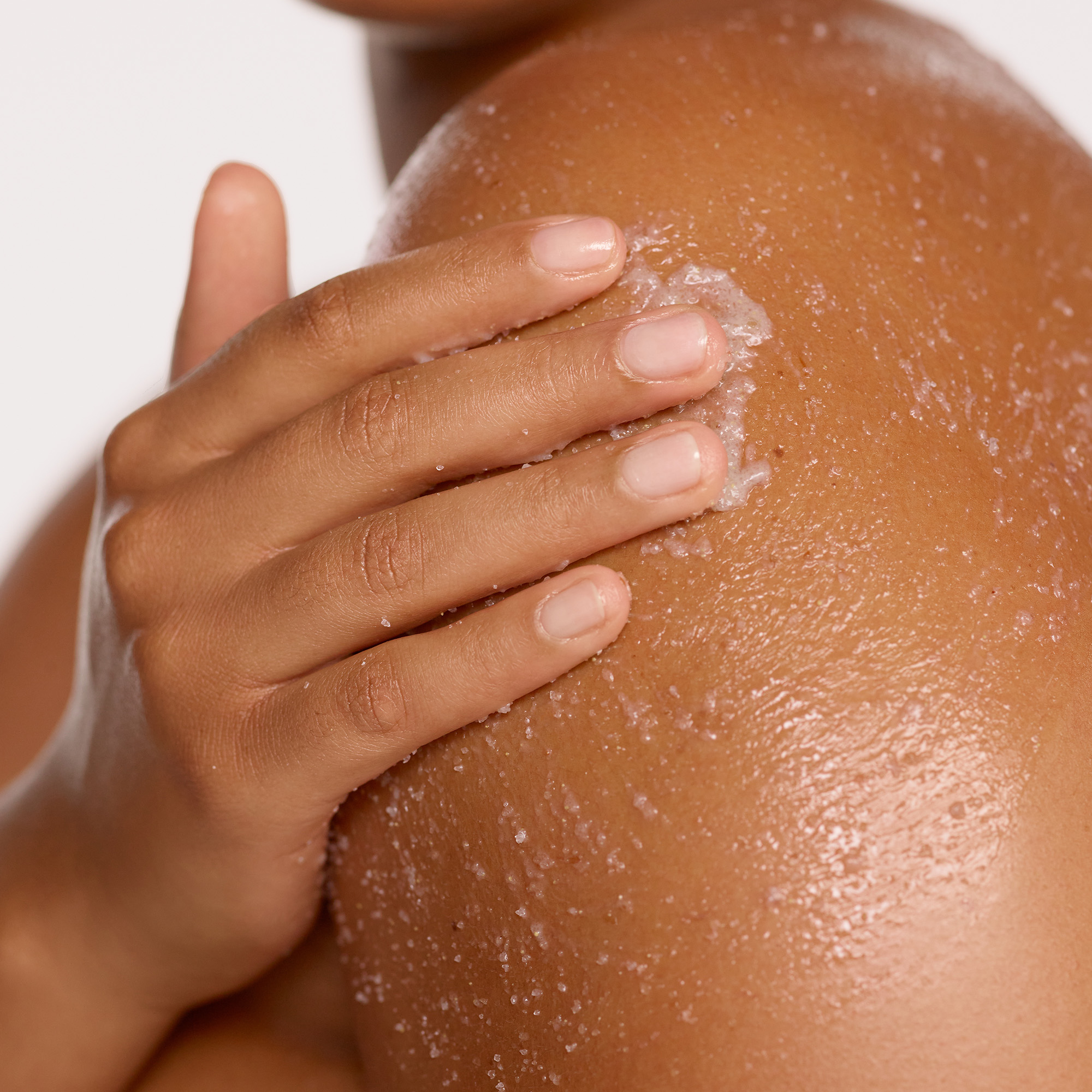 Image of a model using the massaging the Resurfacing & Balancing Body Polish in circular motions to exfoliate and smooth her skin.