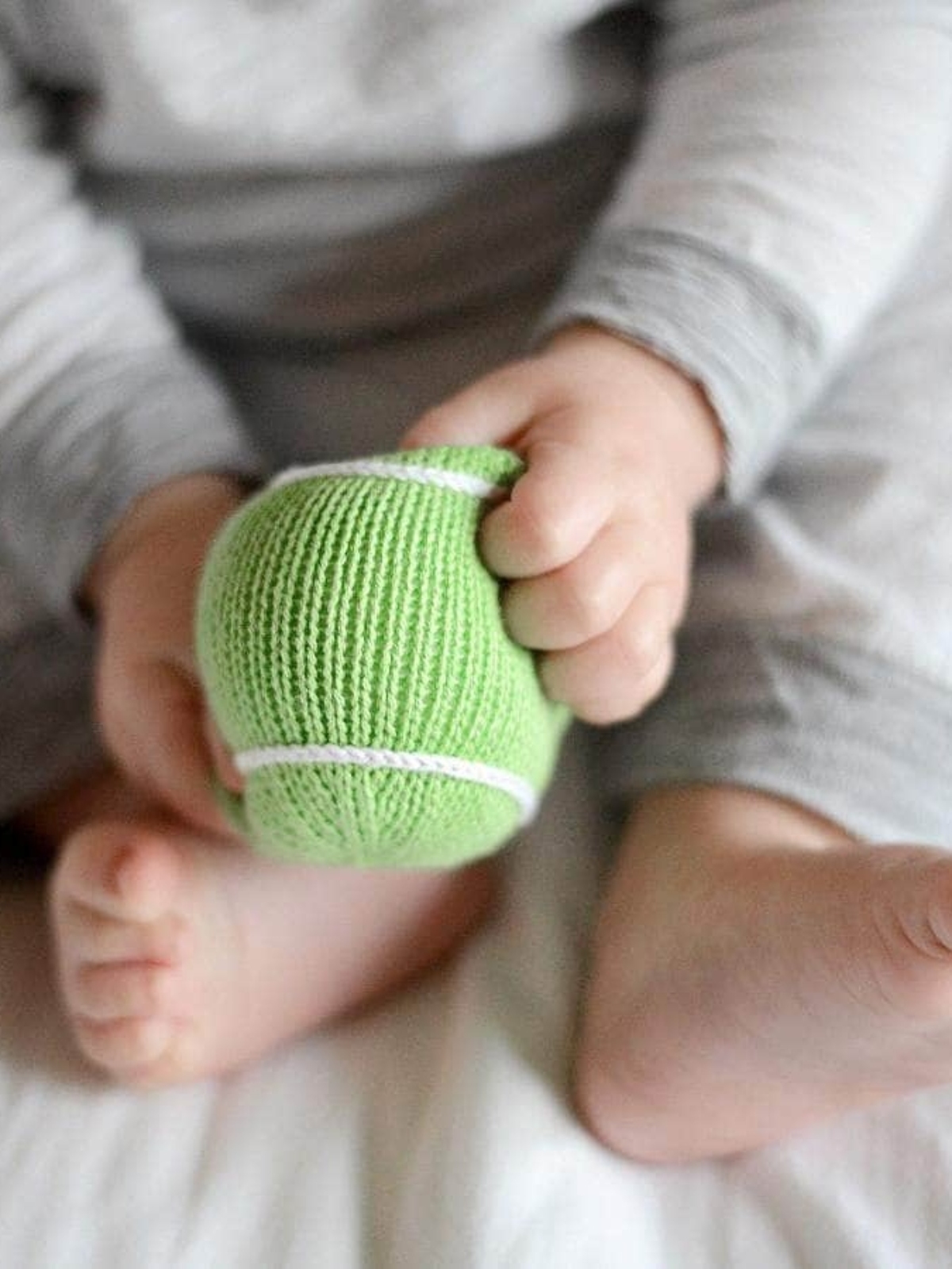 infant holding tennis ball rattle