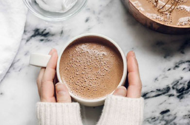 Hands holding a mug of hot cocoa made with Navitas Keto Cacao Powder