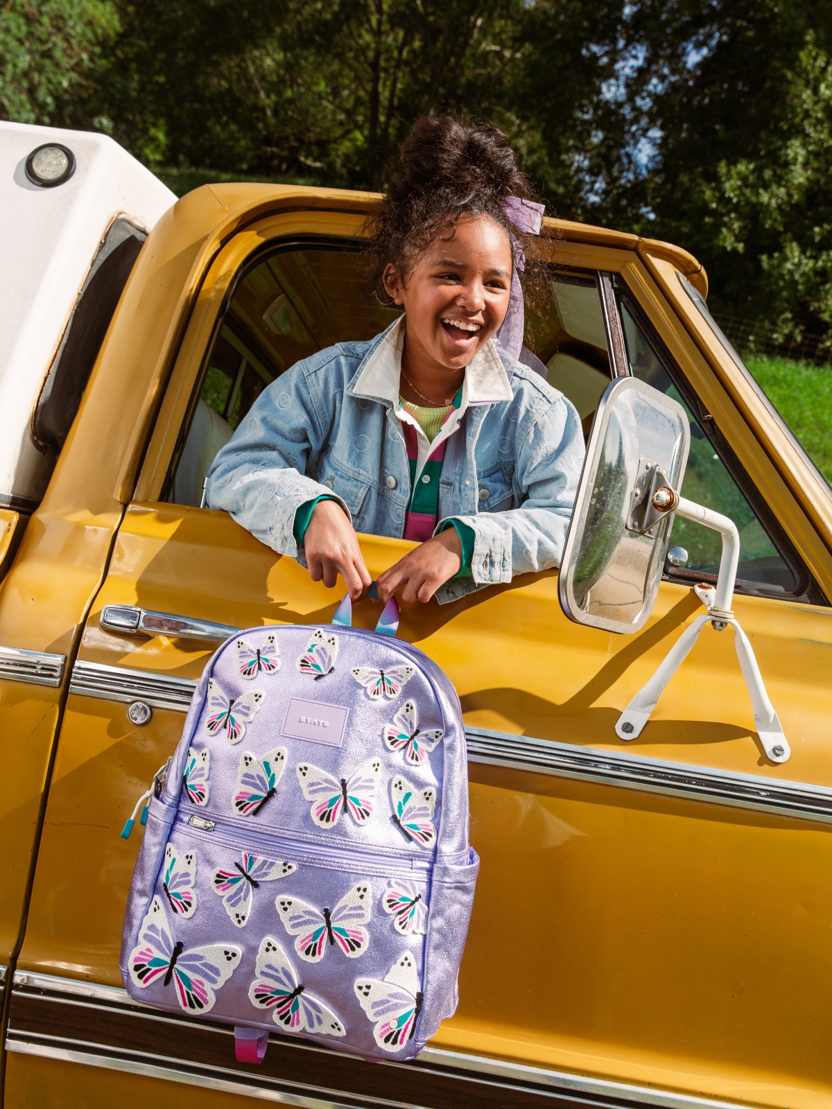 girl holding butterfly backpack outside of car window