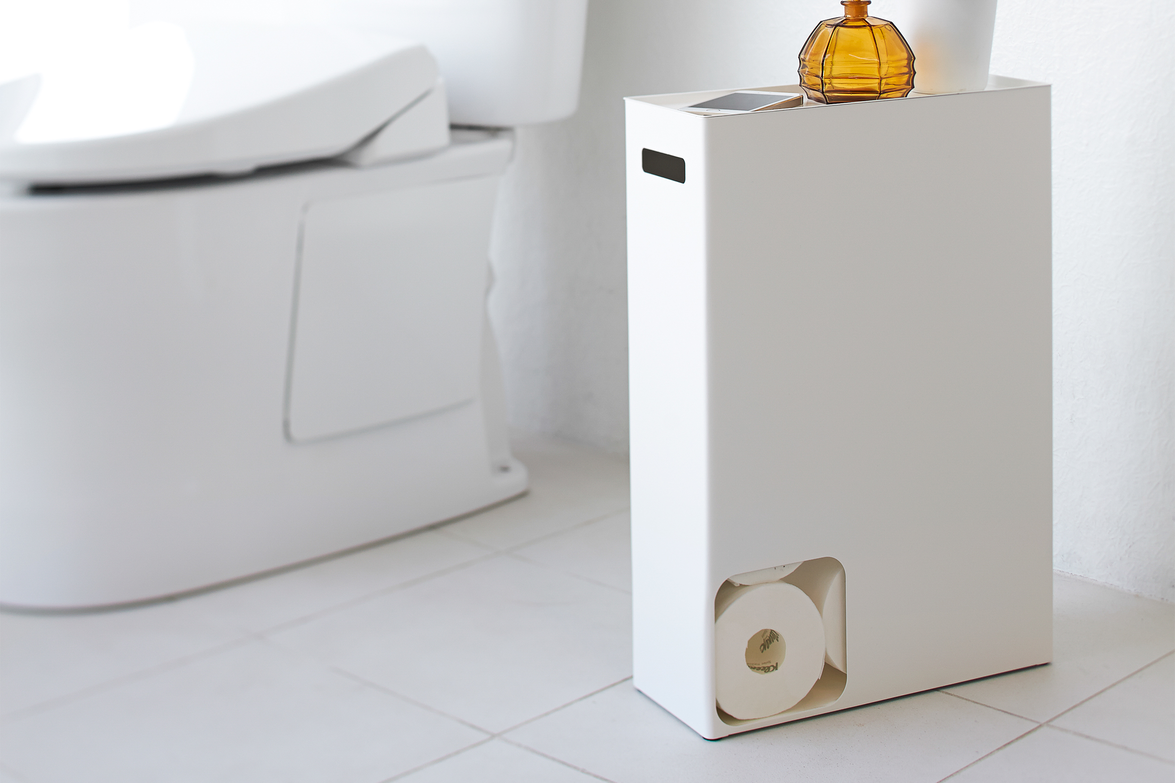Vorderansicht des weißen Toilettenpapierhalters von Yamazaki Home mit Toilettenpapier und Dekorationsartikeln im Badezimmer.