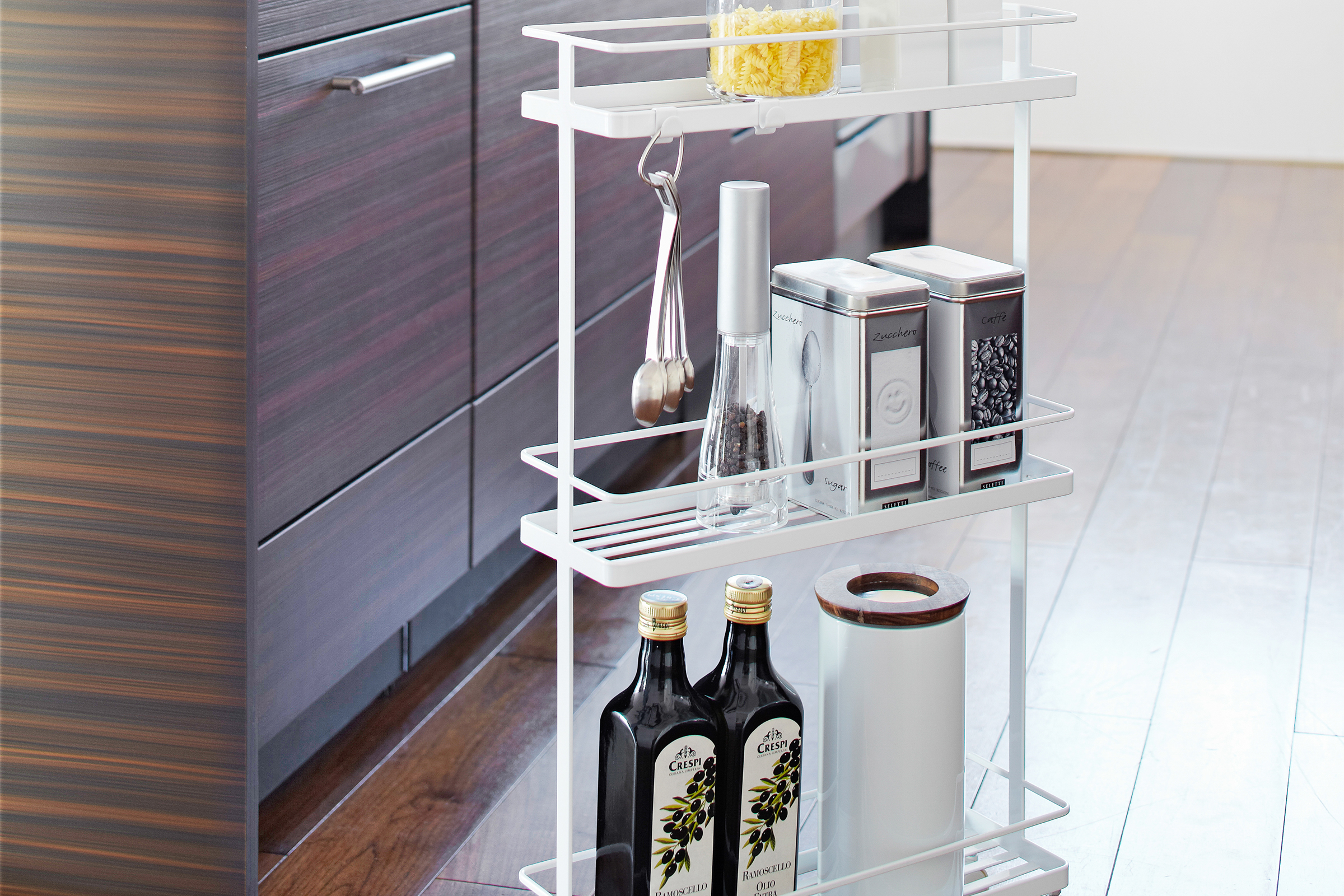 Front view of Yamazaki Home white Rolling Cart holding spices, oils, and cooking accessories in kitchen.