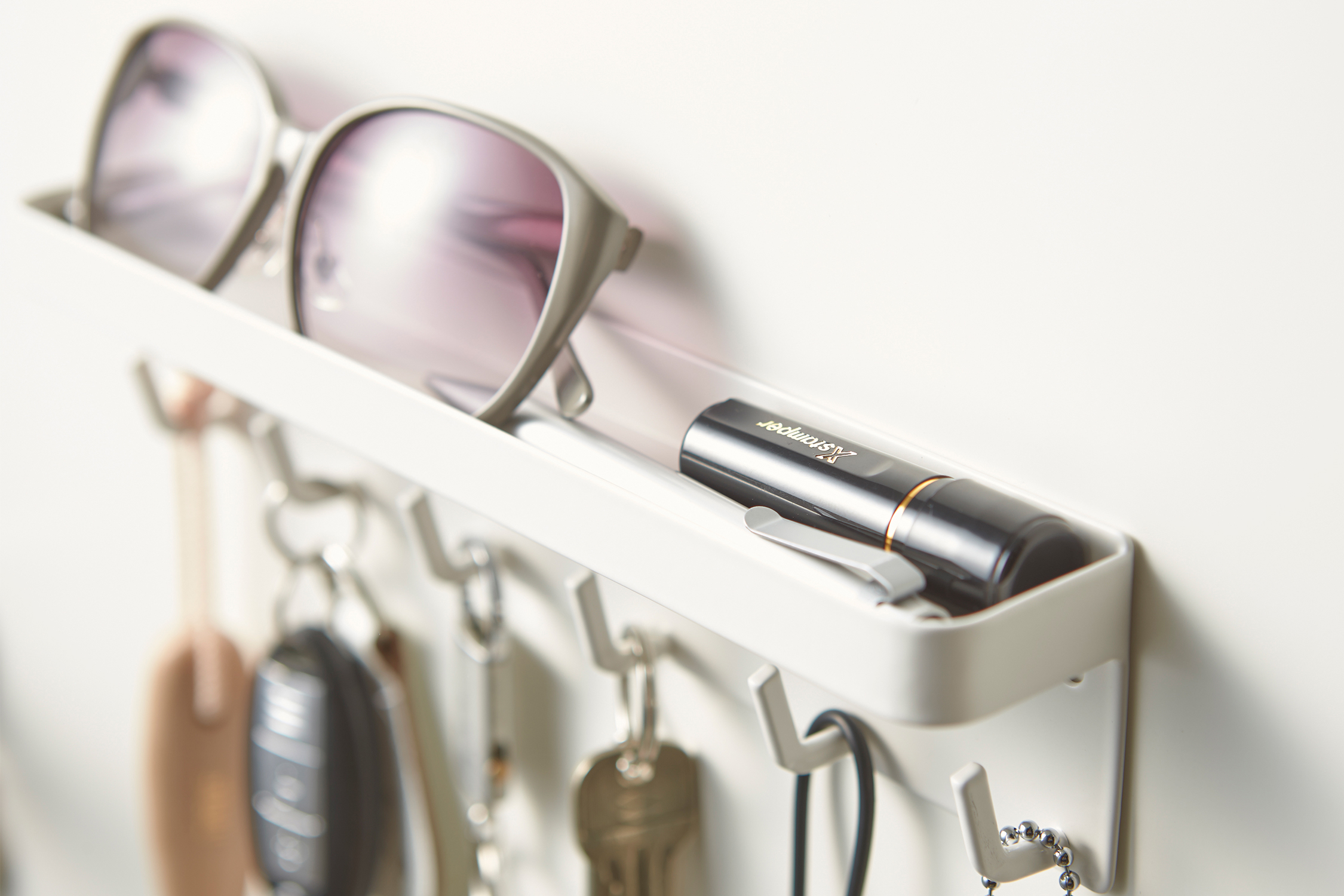 Close up side view of Yamazaki Home white Magnetic Key Holder holding keys, sunglasses, and items.