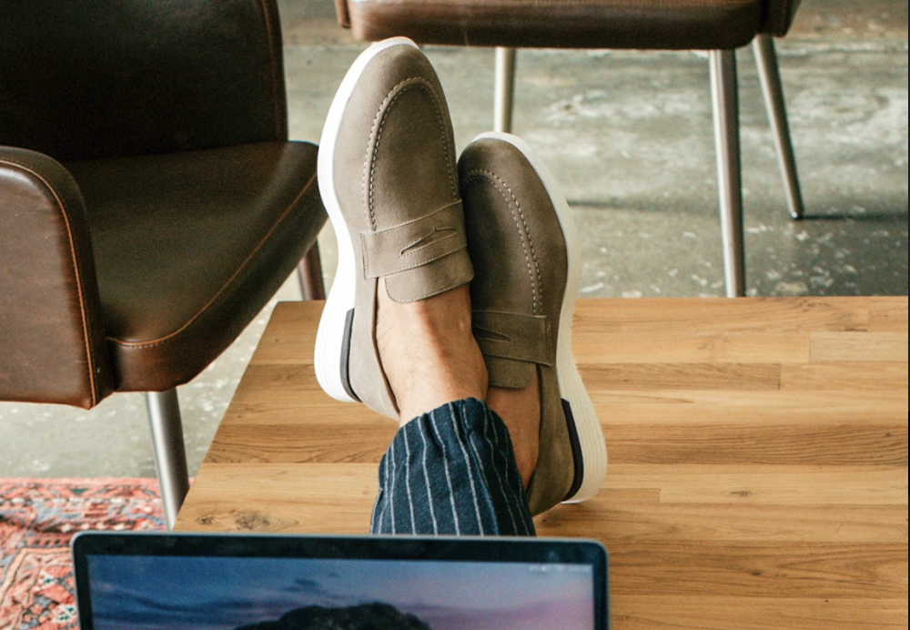 Knee down view of man resting his feet on a coffee table wearing Hybrid Dress shoe Crossover Loafer in Stone