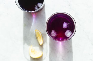 Wellness shots made with Navitas Superfood+ Berry Blend next to lemon slices