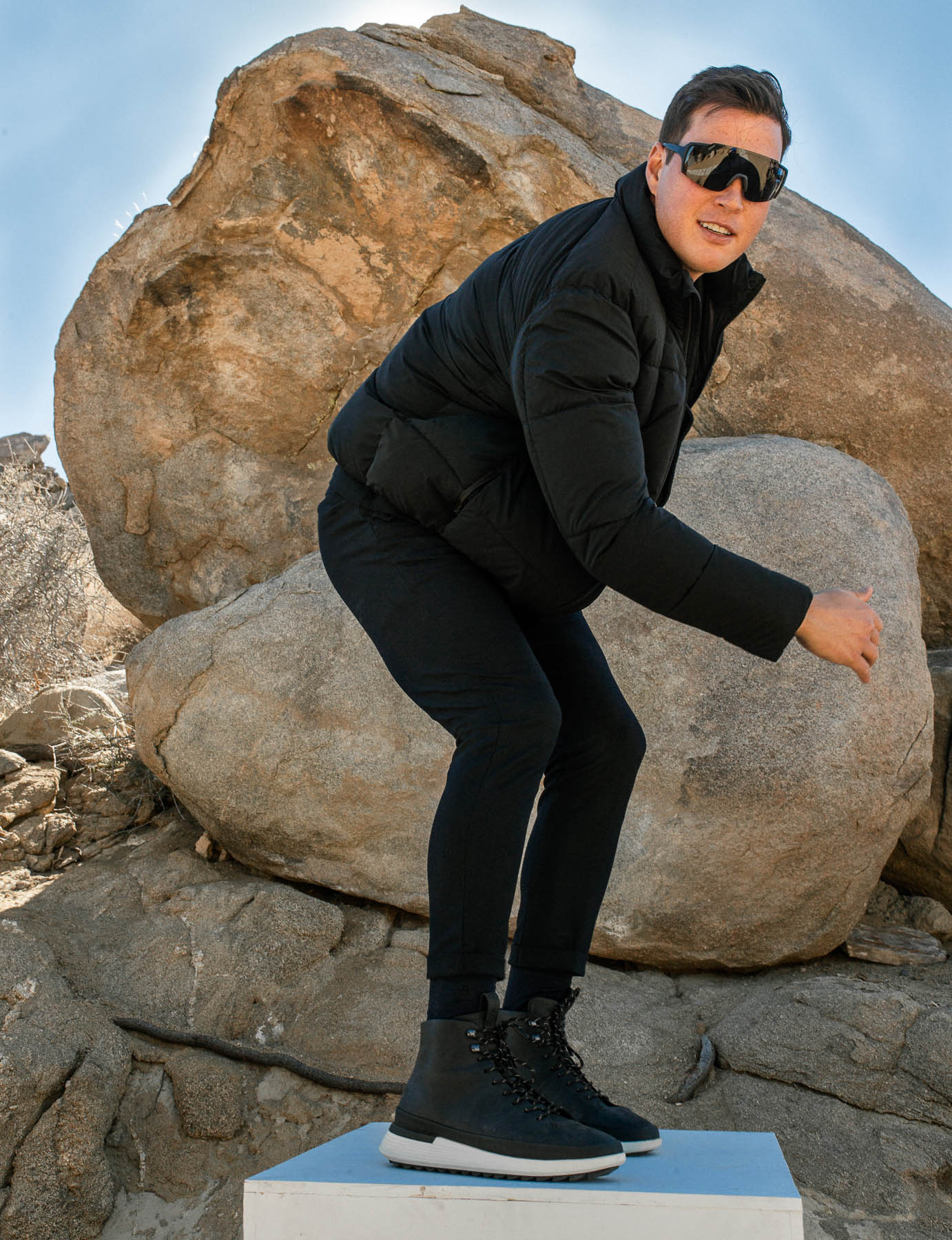 Man standing on a pedestal wearing wearing Men's boot Crossover Hiker WTZ in Navy with large rocks in the background