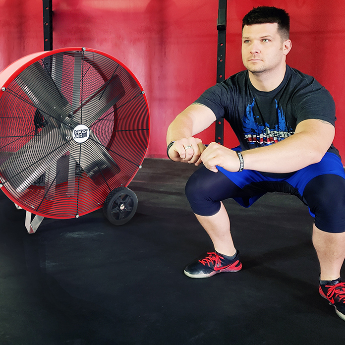 Drum fan cools a client during a CrossFit workout at a gym.