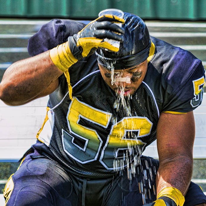 An athlete tries to keep cool on a hot day with a cup of water. Misting fans are a great tool for sports rehab and use an ultra-fine mist to effectively help players cool off.