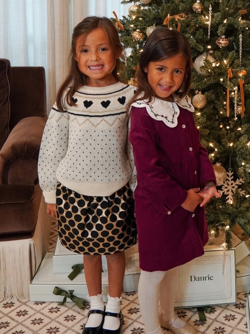two girls wearing holiday outfits in front of christmas tree