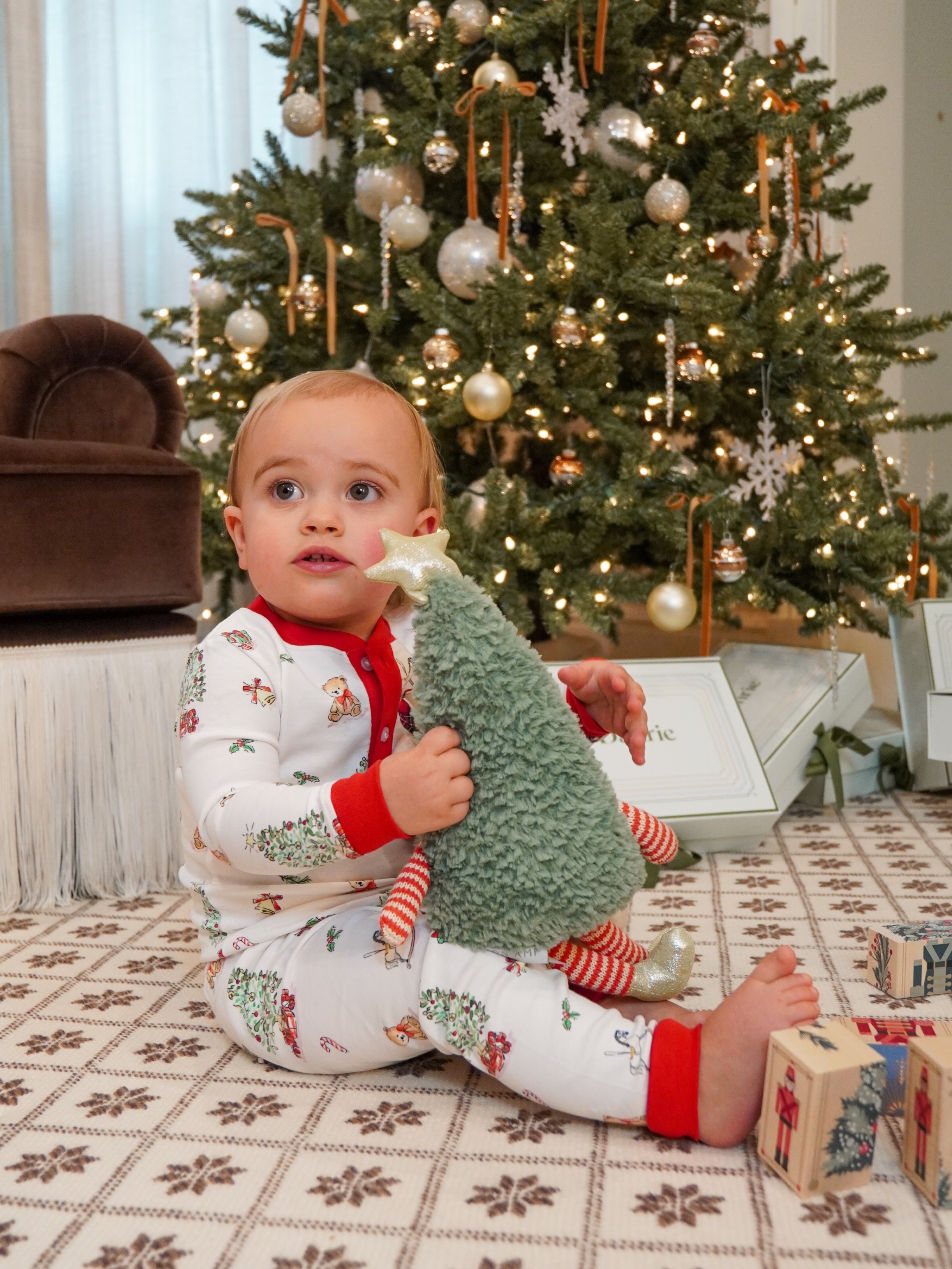 baby wearing christmas pajamas in front of christmas tree