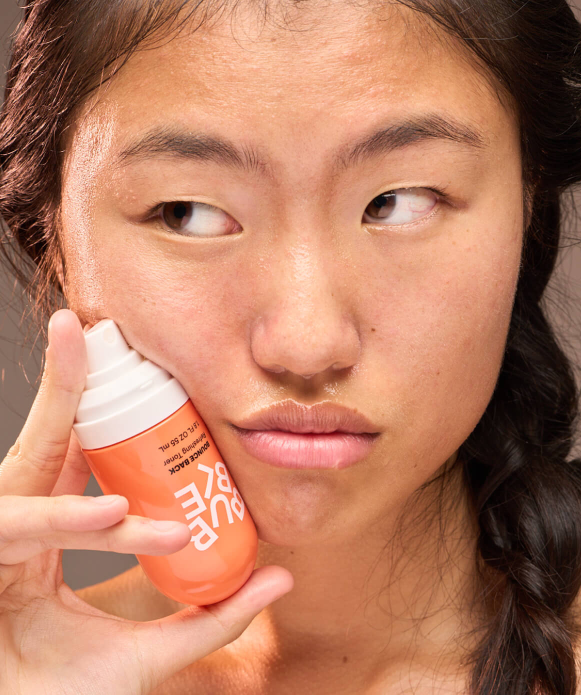 Asian young woman holding a spray-on toner for all skintypes. Good when oil or shine pop up. Free of alcohols, parabens, artificial color & added fragrance materials. Cruelty-free and vegan.