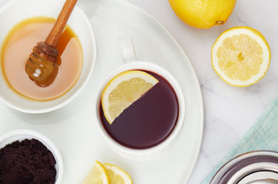 Mug of elderberry tea made with Navitas Elderberry Powder on a tray next to honey and lemons