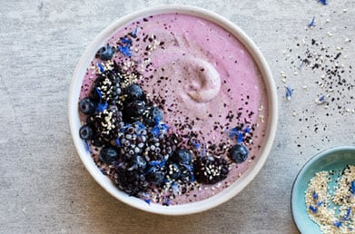 Glass of elderberry smoothie made with Navitas Elderberry Powder and topped with fresh ingredients