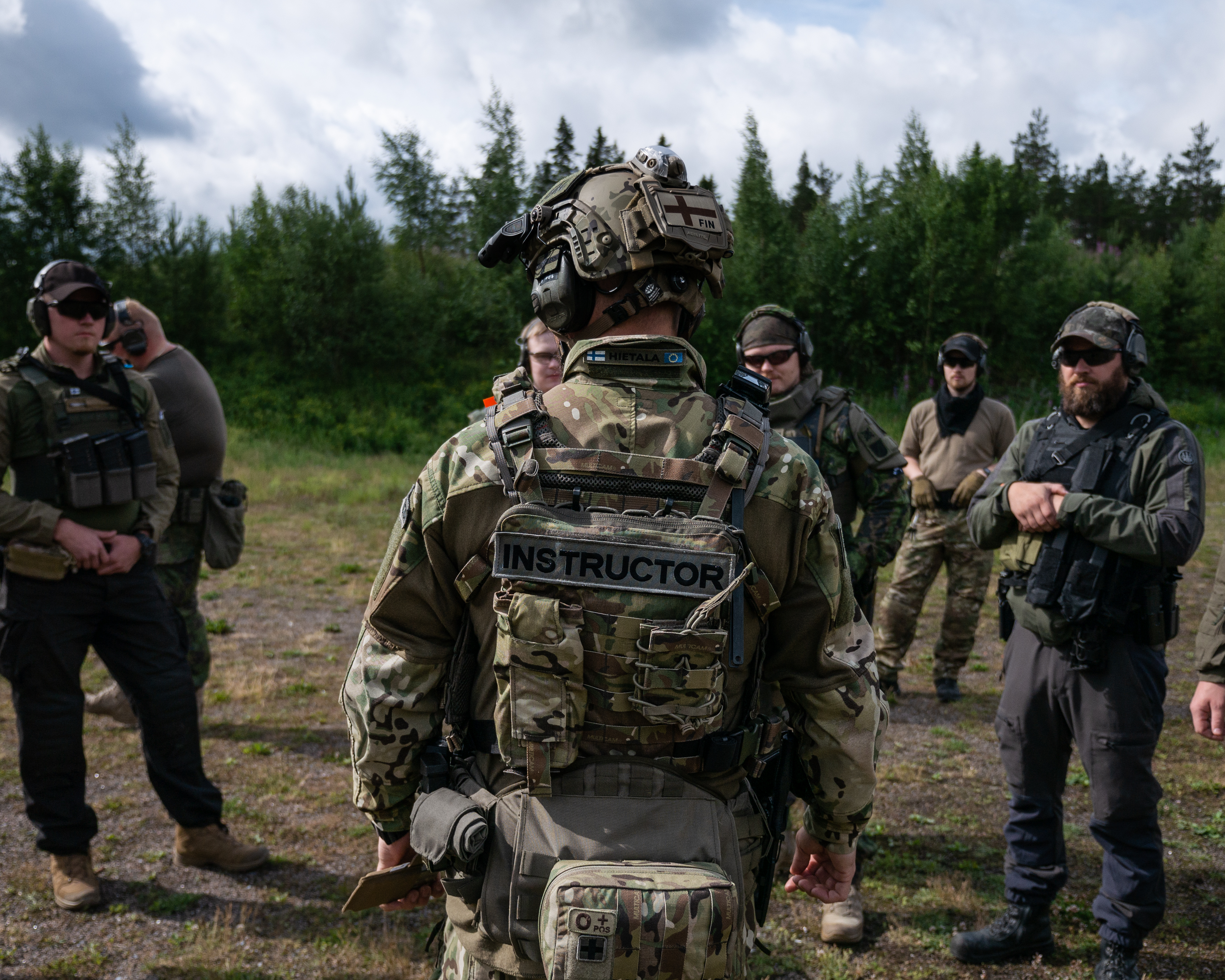 Men are standing around instructor Jere Hietala. They are on a shooting range. The men are wearing tactical clothing. 