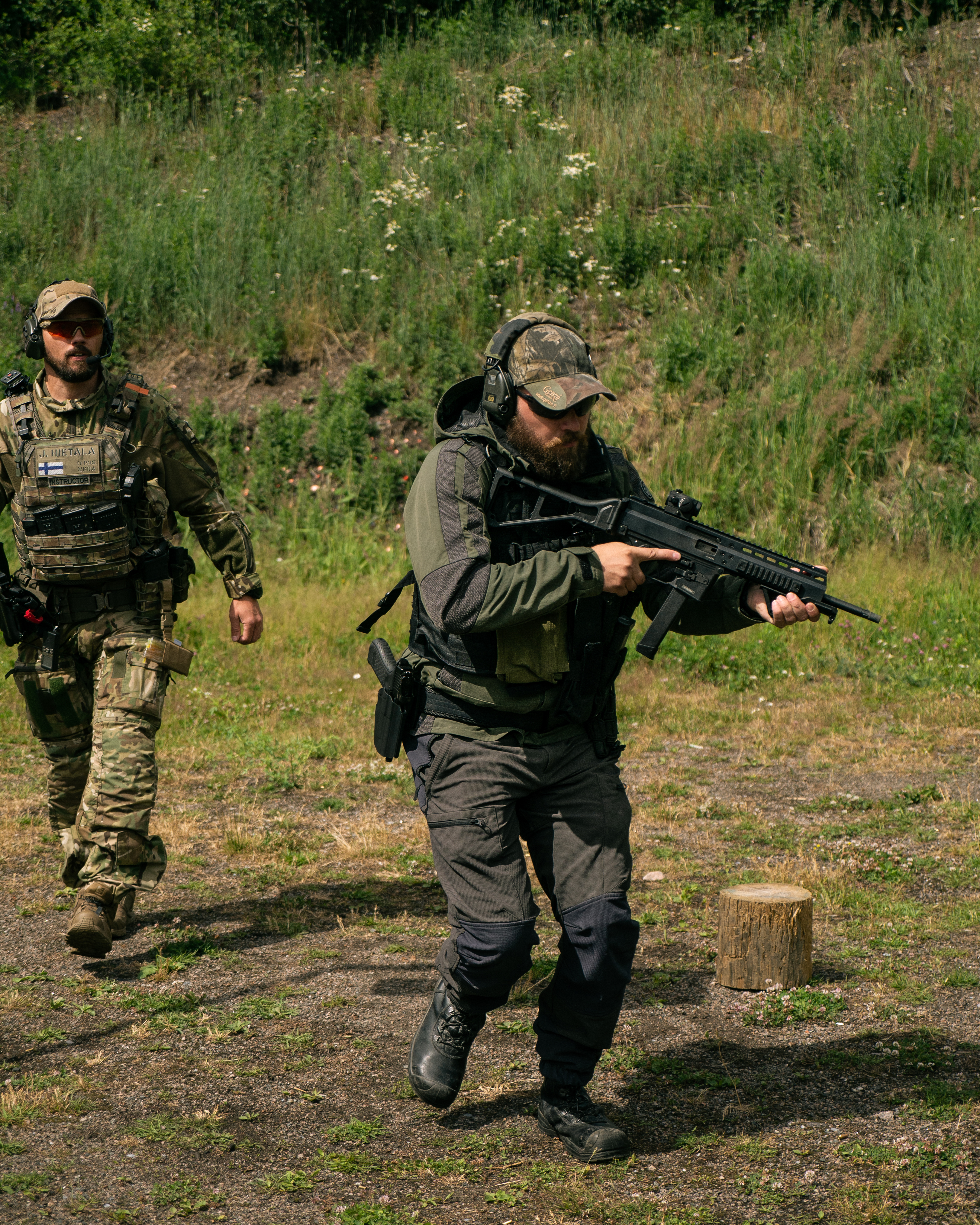 Man shooting a rifle. The rifle has a red dot on it. The man is a jacket. He is on a shooting range.