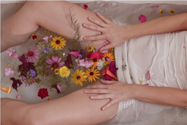 The bottom half of a woman in the water with flowers surrounding her.