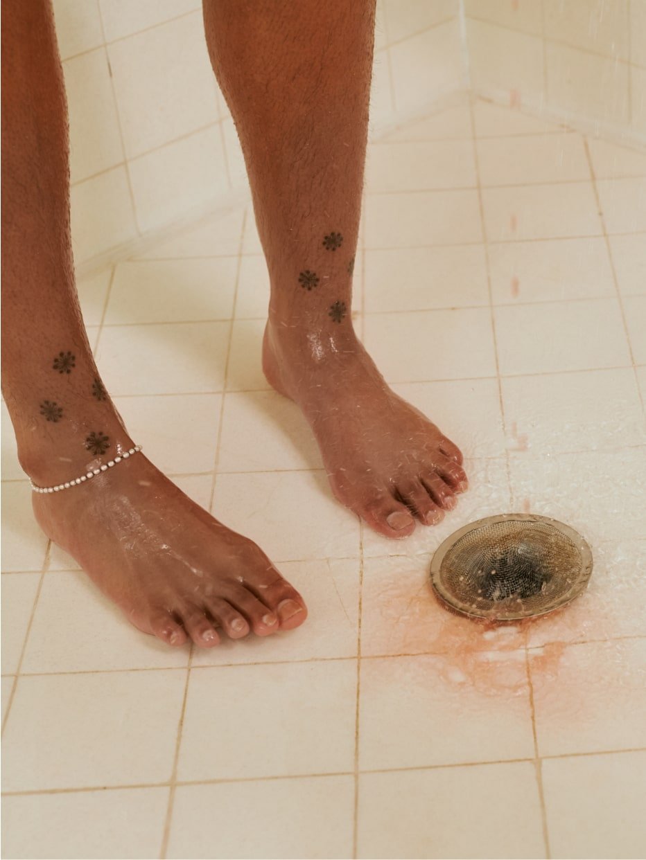 A close up of a person's feet inside a shower with liquid flowing into the drain