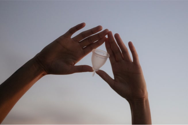 Two hands holding a menstrual cup in the air.